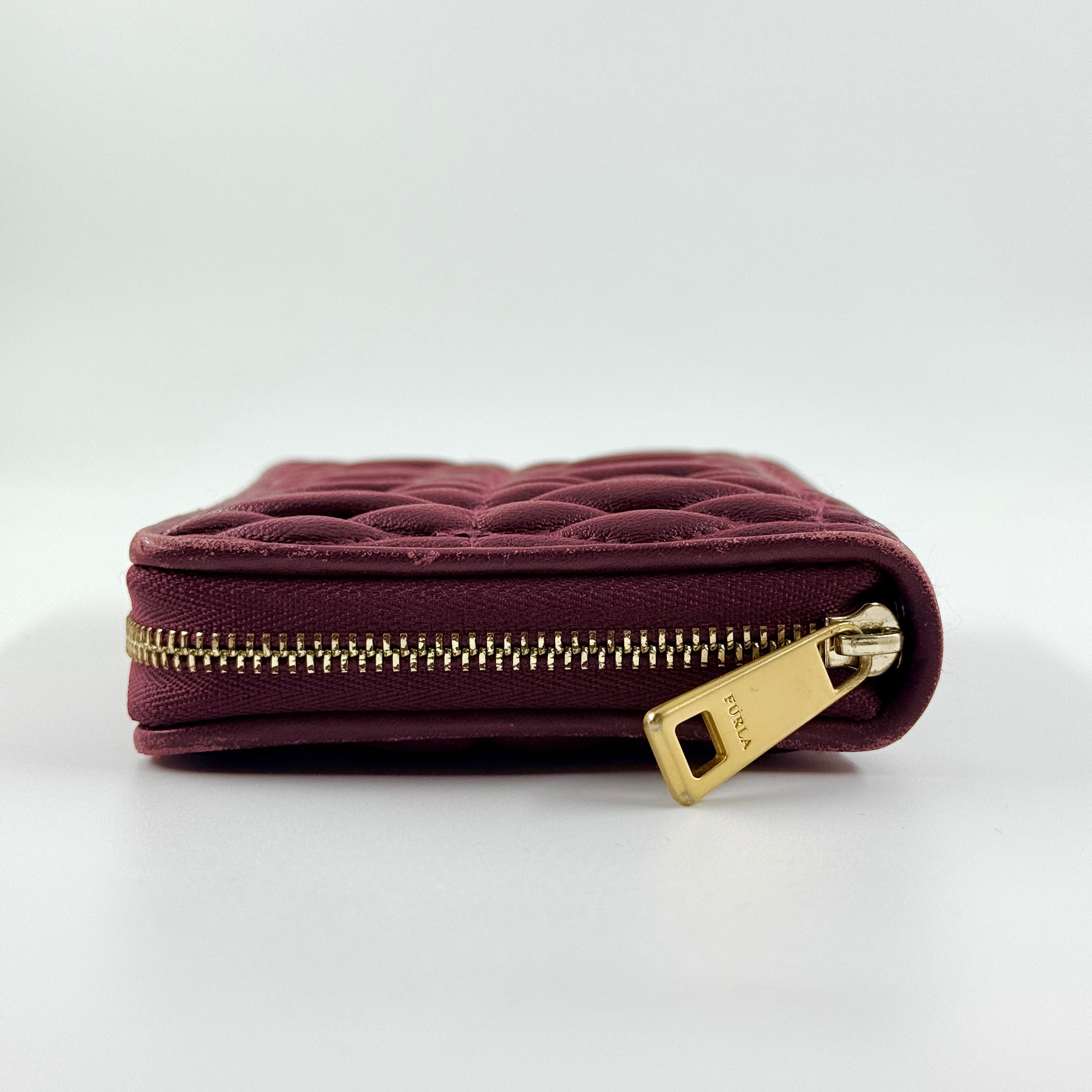 Furla quilted Cometa zip around wallet in deep burgundy leather with gold-tone hardware and diamond stitching.