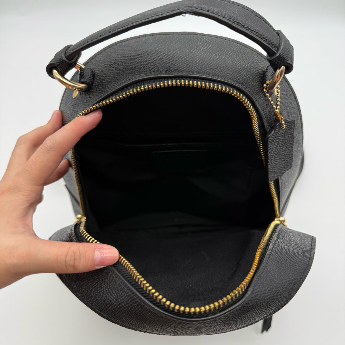 Coach Jordyn Leather Backpack in black grained leather with gold-tone hardware and minimal branding, photographed on white background.