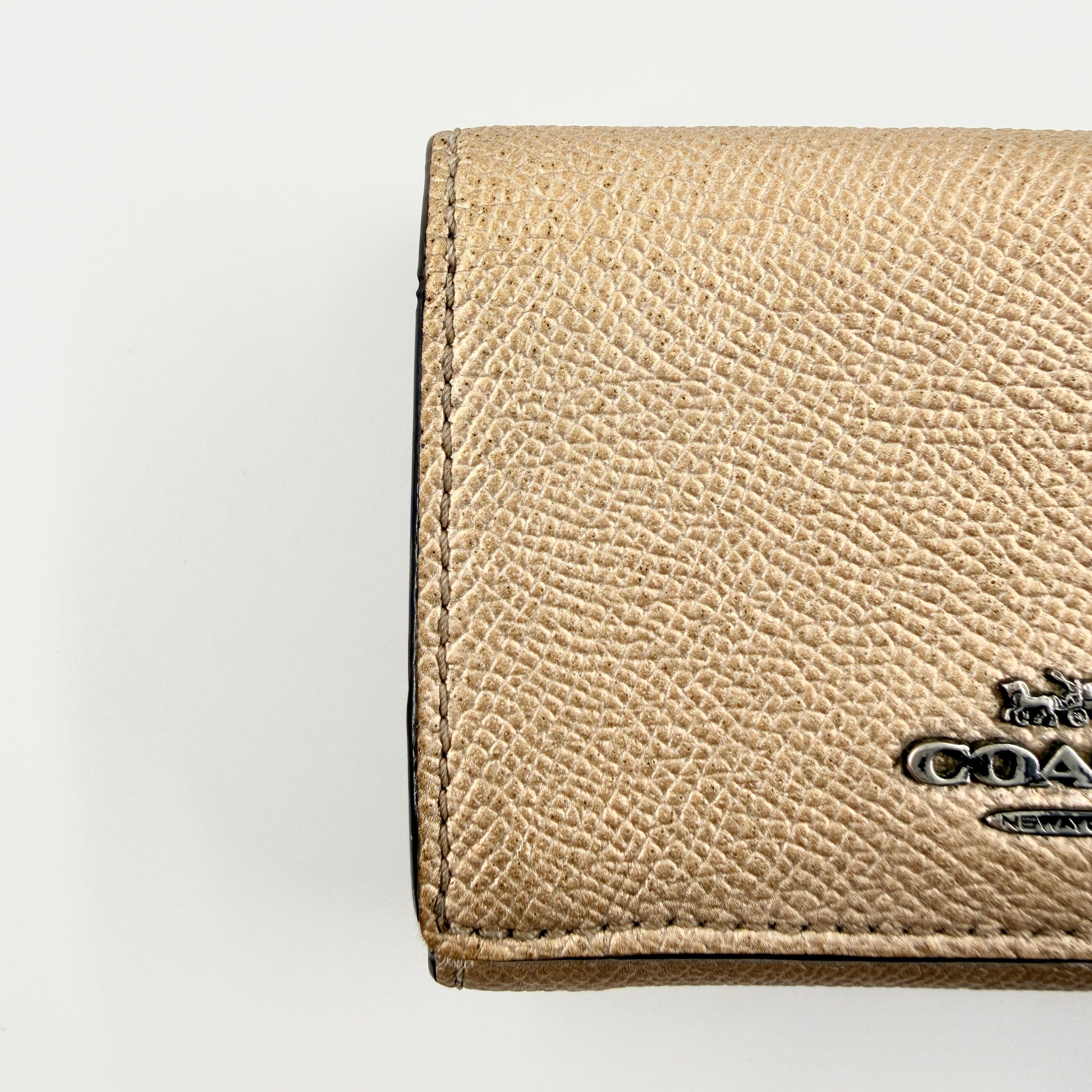 Coach metallic gold small flap wallet with silver logo plaque and crosshatch textured leather.