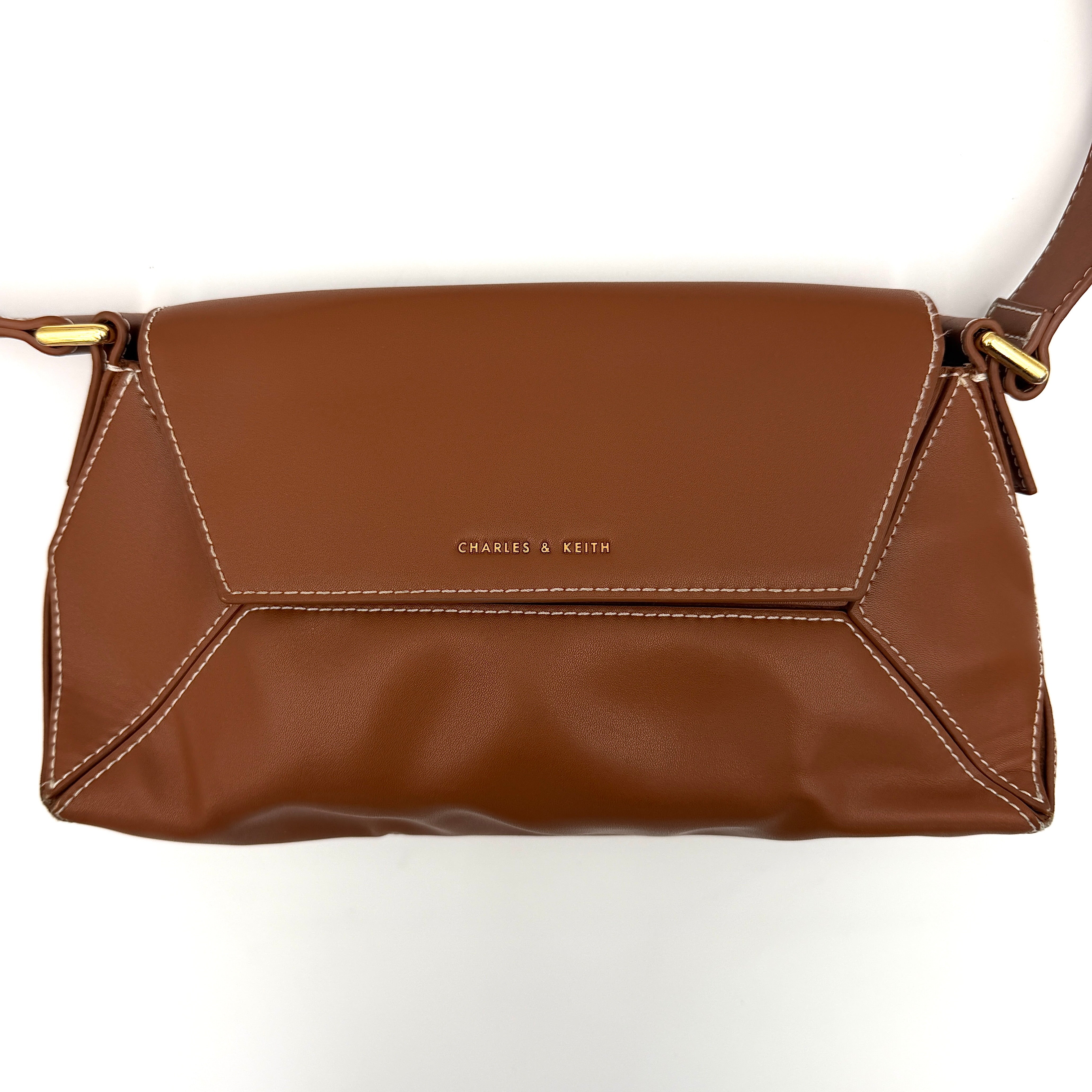 Charles & Keith Nasrin Geometric Crossbody Bag in brown faux leather with angular stitching, gold-tone hardware, and adjustable strap.