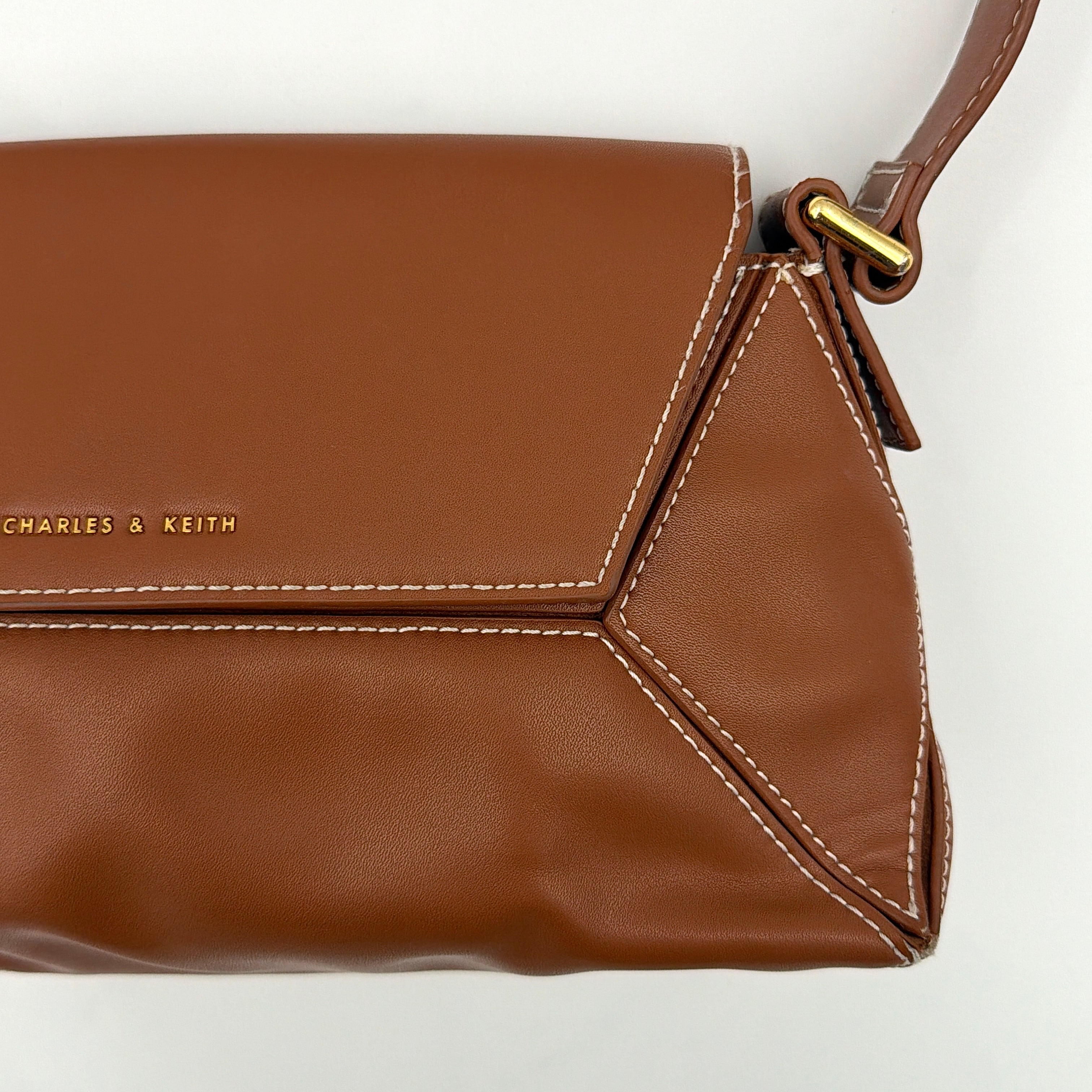 Charles & Keith Nasrin Geometric Crossbody Bag in brown faux leather with angular stitching, gold-tone hardware, and adjustable strap.