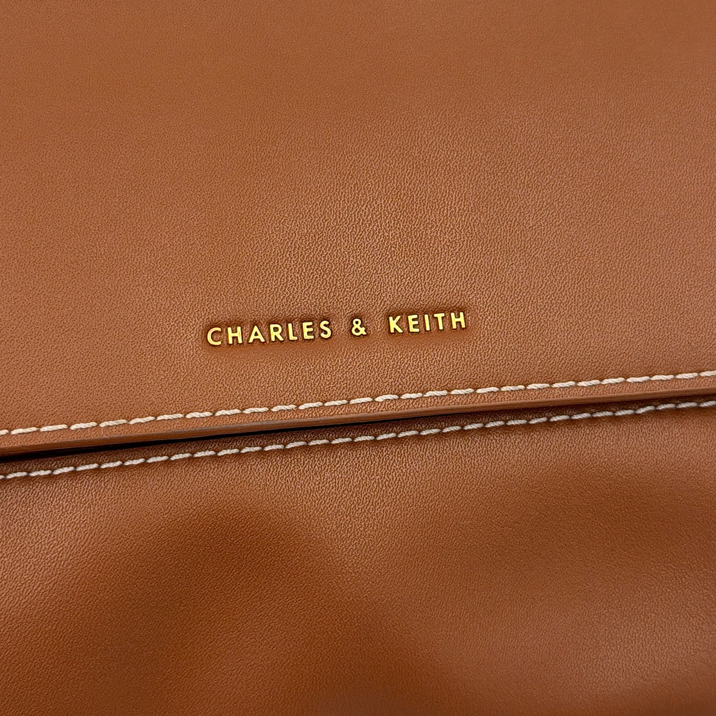 Charles & Keith Nasrin Geometric Crossbody Bag in brown faux leather with angular stitching, gold-tone hardware, and adjustable strap.