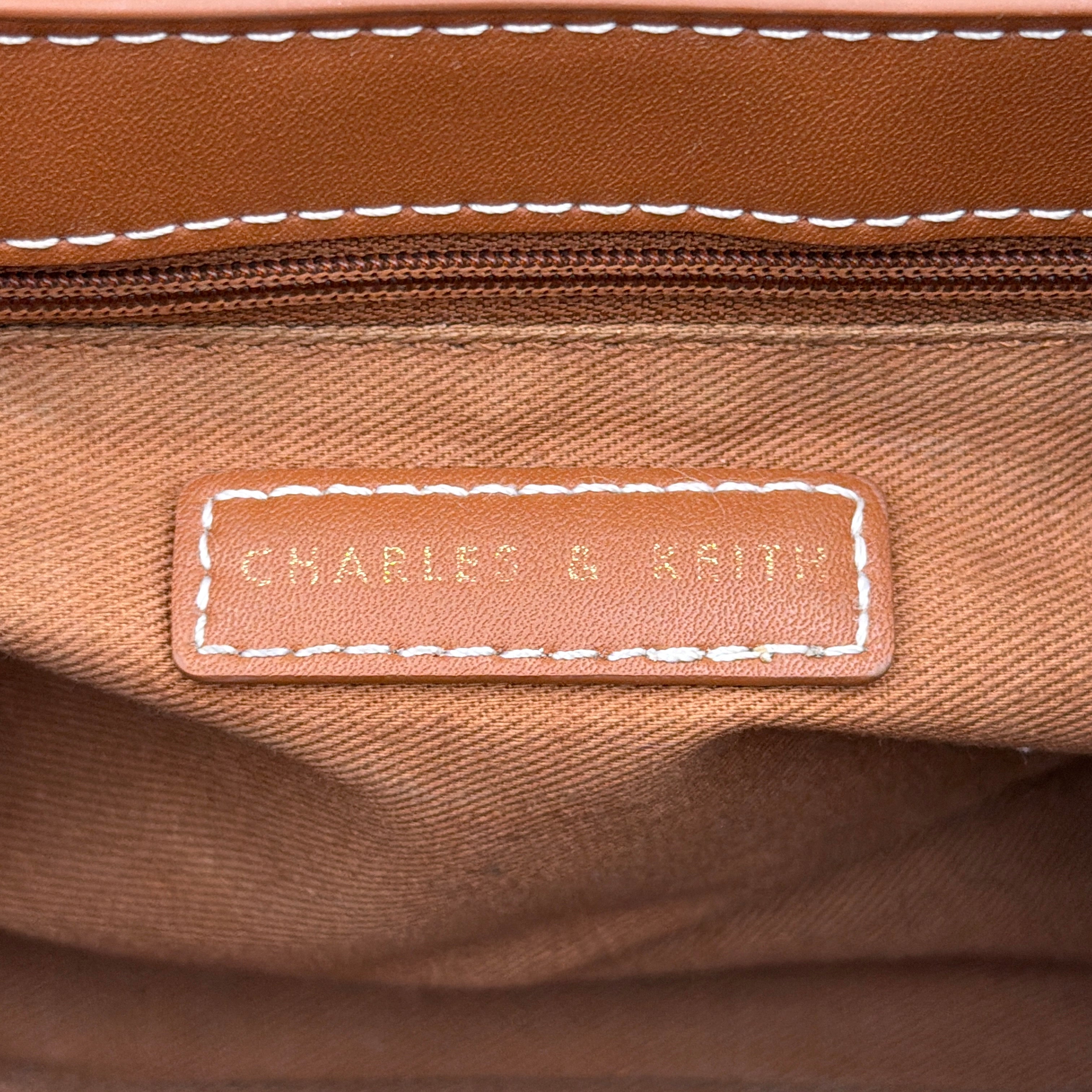 Charles & Keith Nasrin Geometric Crossbody Bag in brown faux leather with angular stitching, gold-tone hardware, and adjustable strap.
