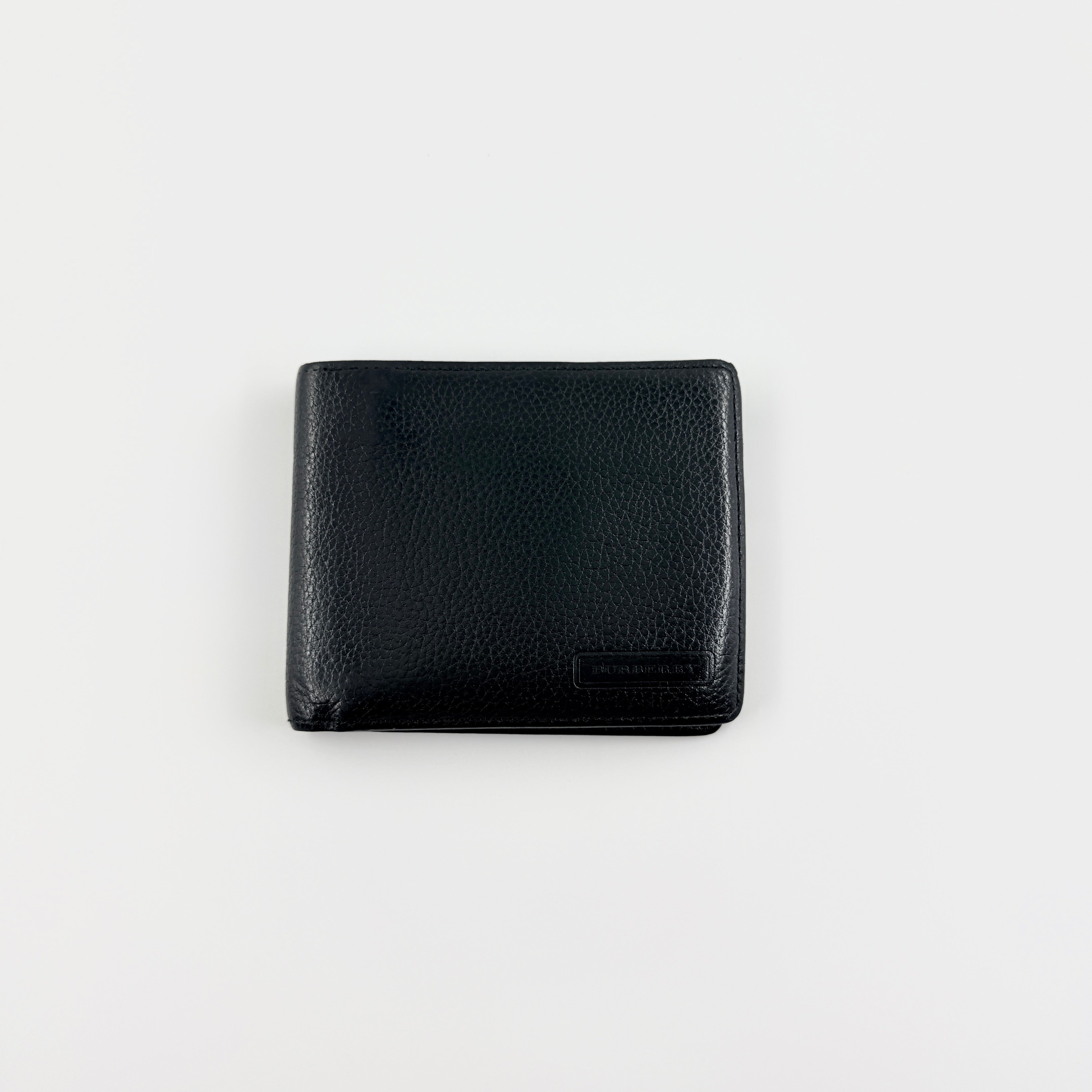 Burberry Nova Check bifold wallet in refined black grained leather with discreet embossed logo, presenting a minimal and polished silhouette.