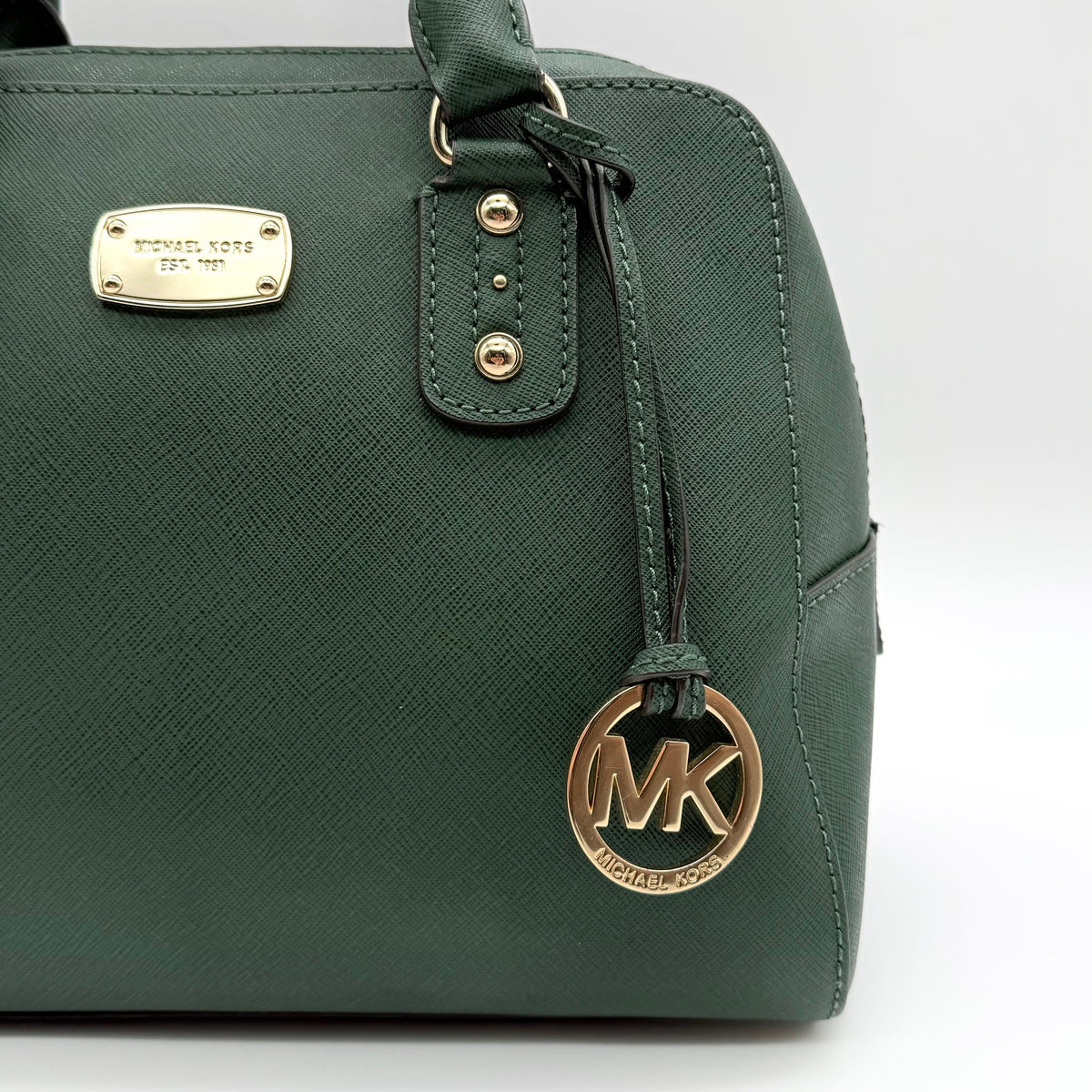 Michael Kors dark green Saffiano leather dome satchel with gold hardware and detachable strap, shown against a white background.
