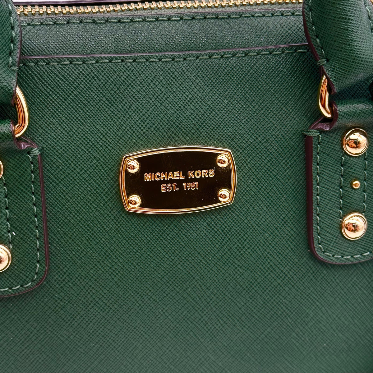 Michael Kors dark green Saffiano leather dome satchel with gold hardware and detachable strap, shown against a white background.