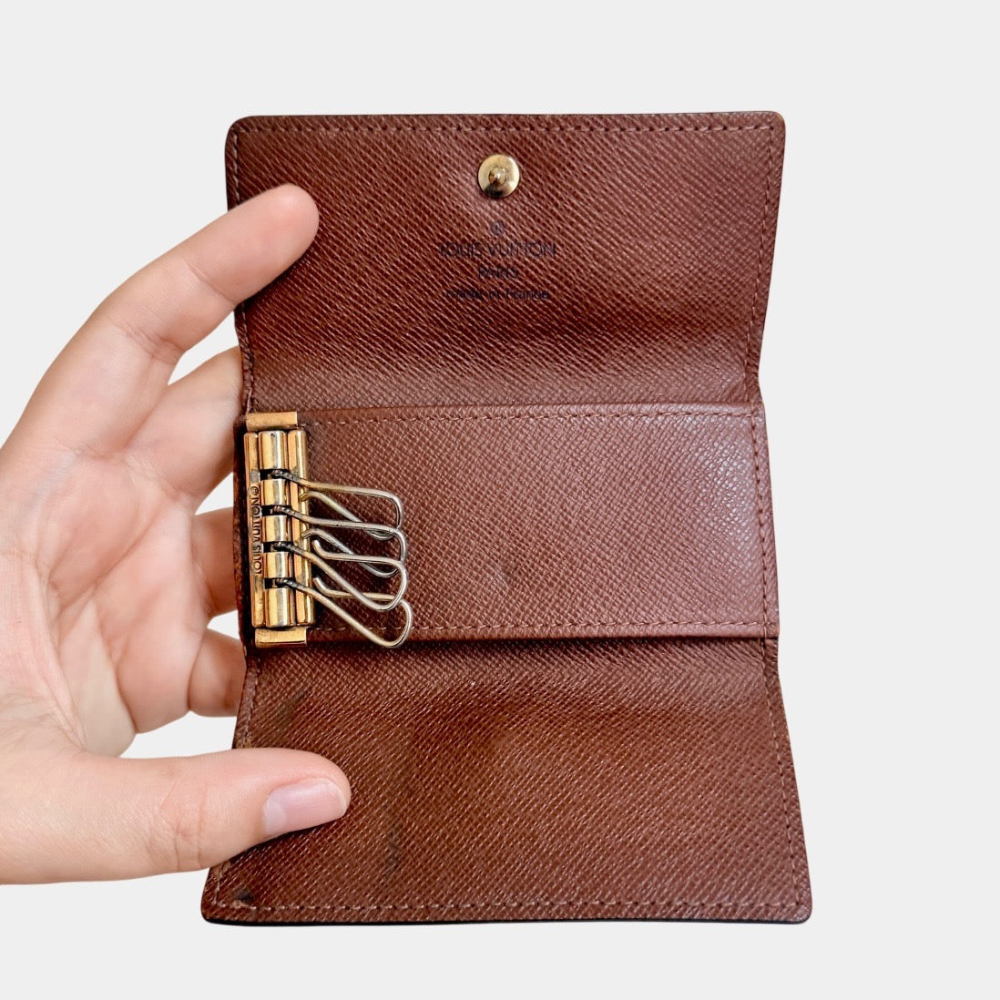 Louis Vuitton monogram key case in brown with gold-tone snap closure and classic LV pattern on coated canvas.