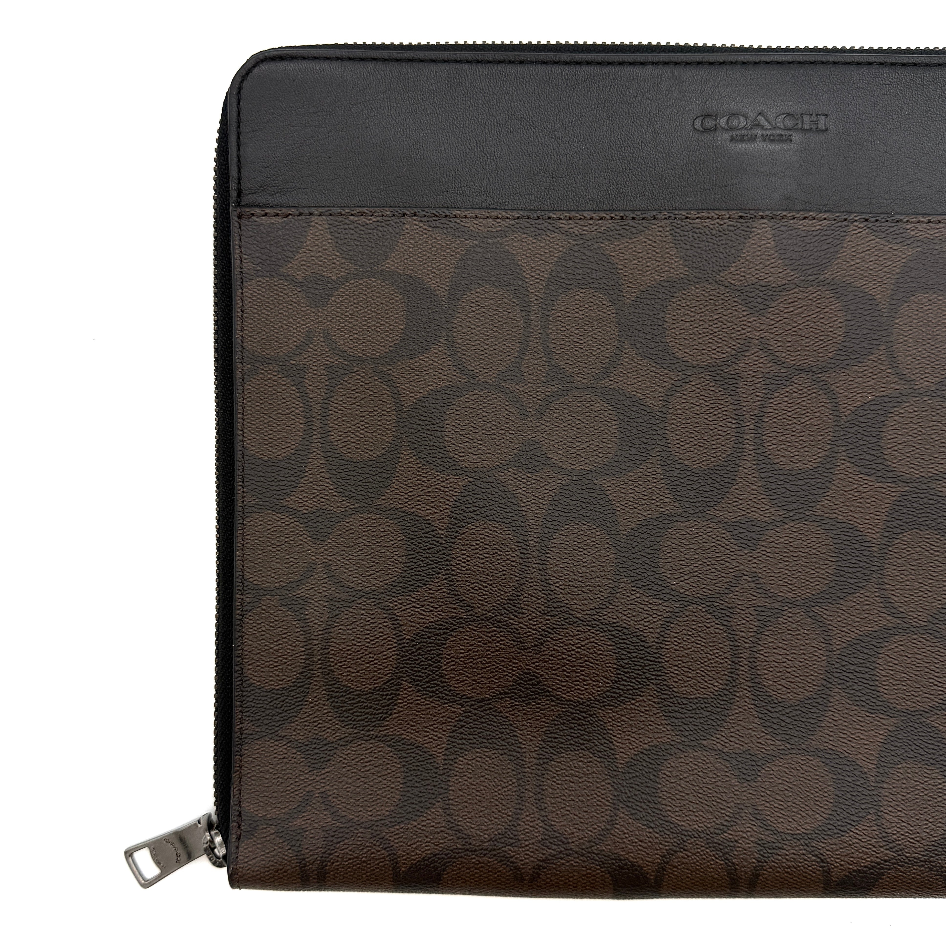 Coach Signature Zip Portfolio in brown and black monogram canvas with zip-around closure, displayed flat against a white background.