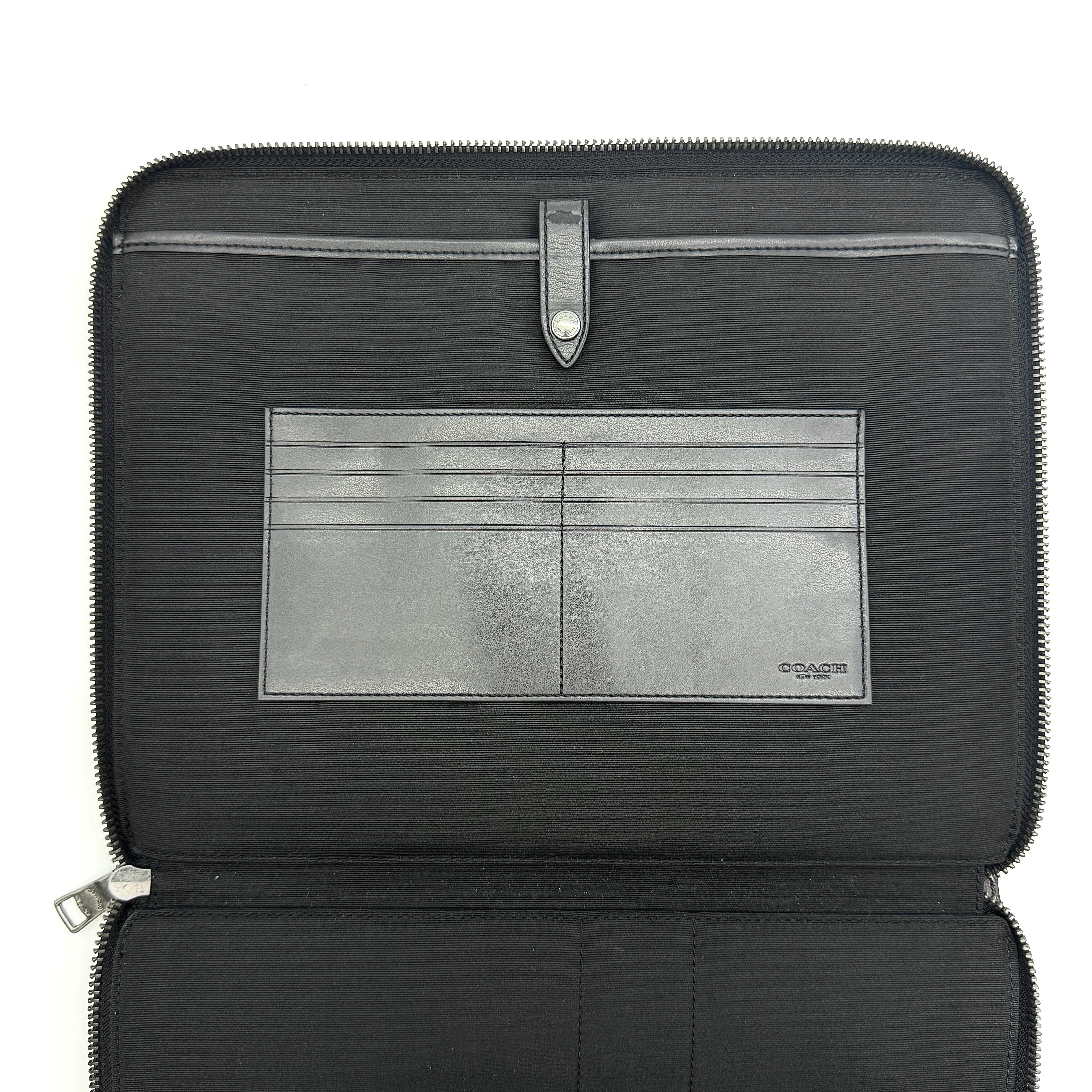 Coach Signature Zip Portfolio in brown and black monogram canvas with zip-around closure, displayed flat against a white background.