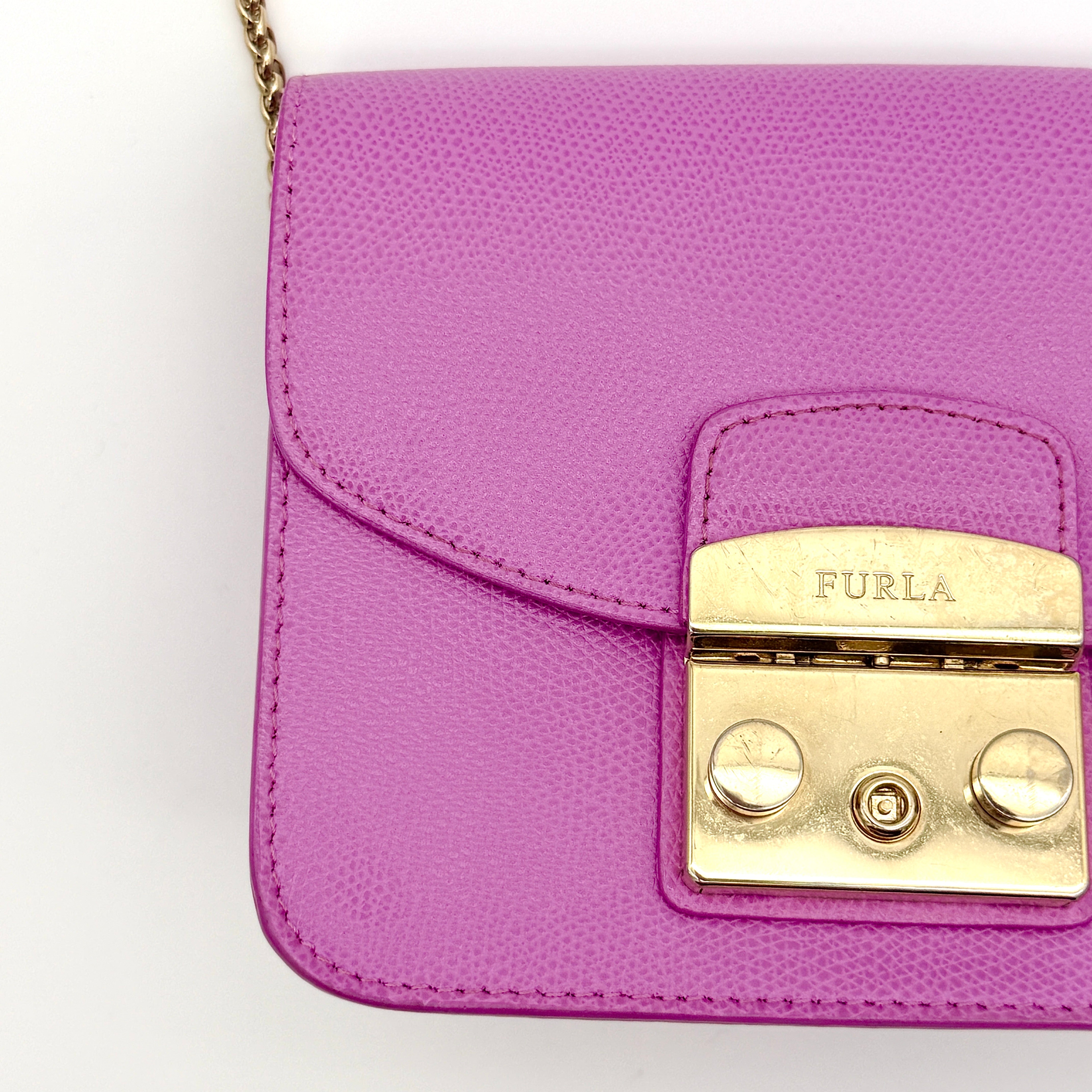 Furla Metropolis crossbody bag in pink grained leather with gold hardware and chain strap, displayed against a white background.