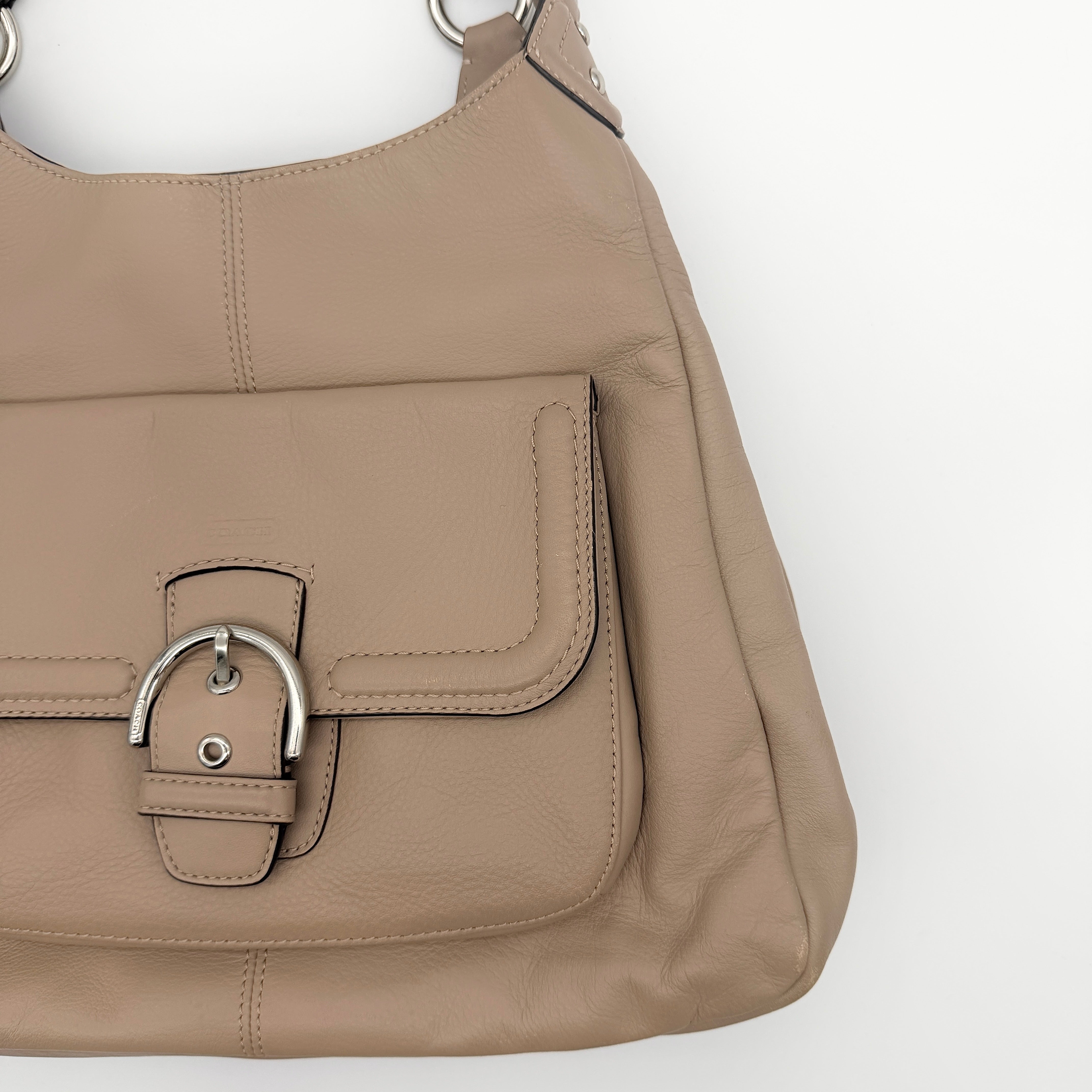 Coach Campbell Hobo shoulder bag in beige leather with silver hardware and front pocket, shown against a white background.