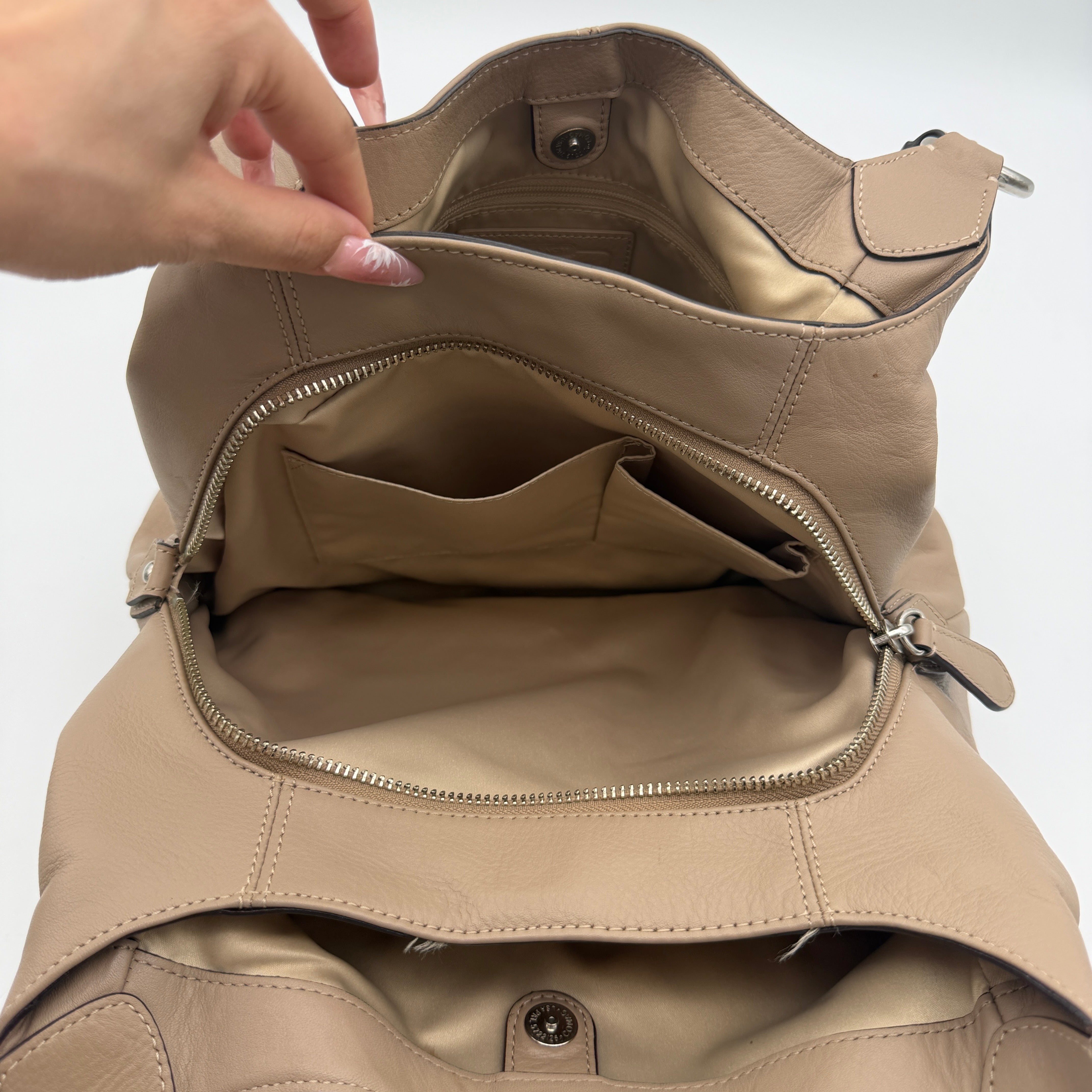 Coach Campbell Hobo shoulder bag in beige leather with silver hardware and front pocket, shown against a white background.