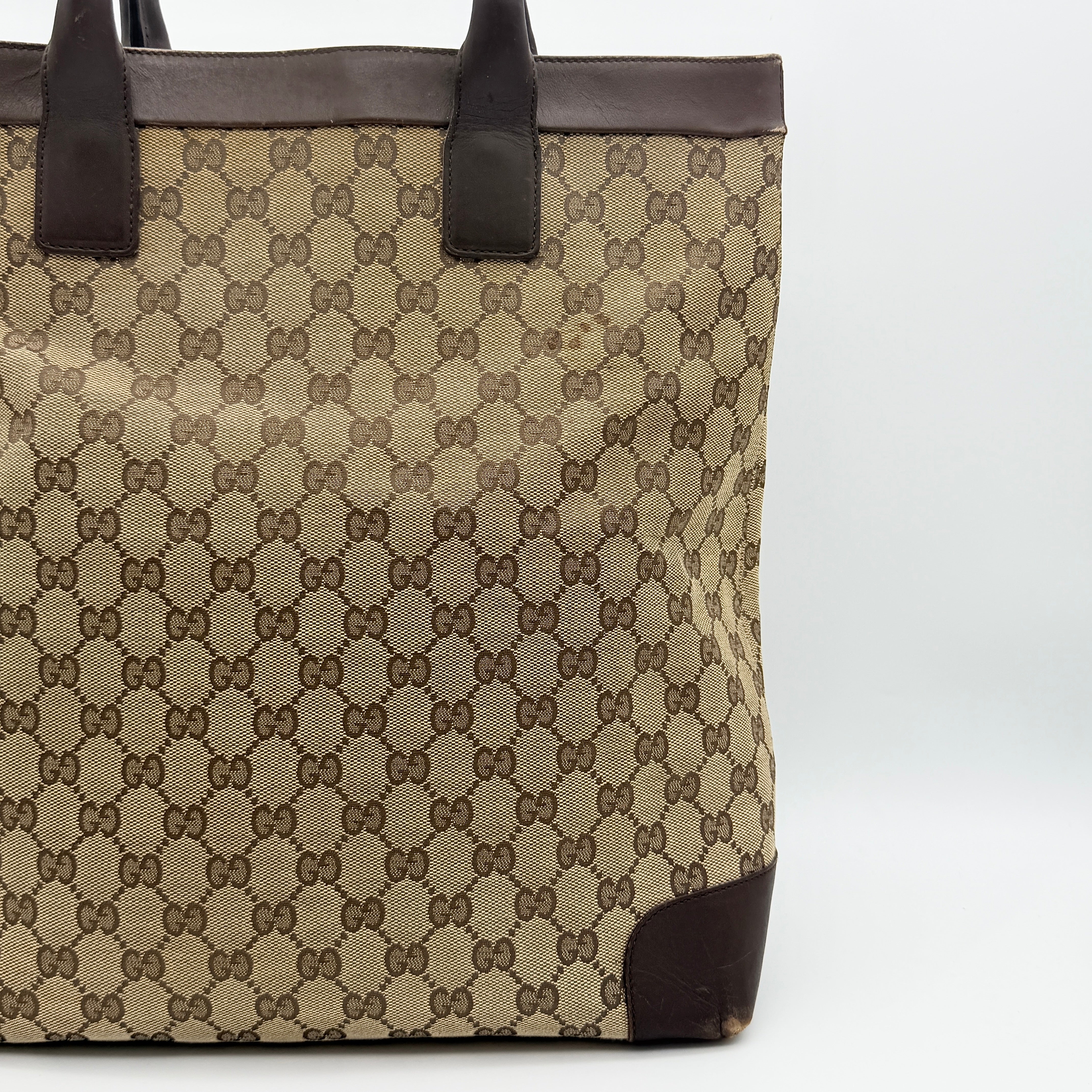 Front view of a Gucci GG Monogram Tote Bag in beige and brown canvas with dark leather trim and structured handles.