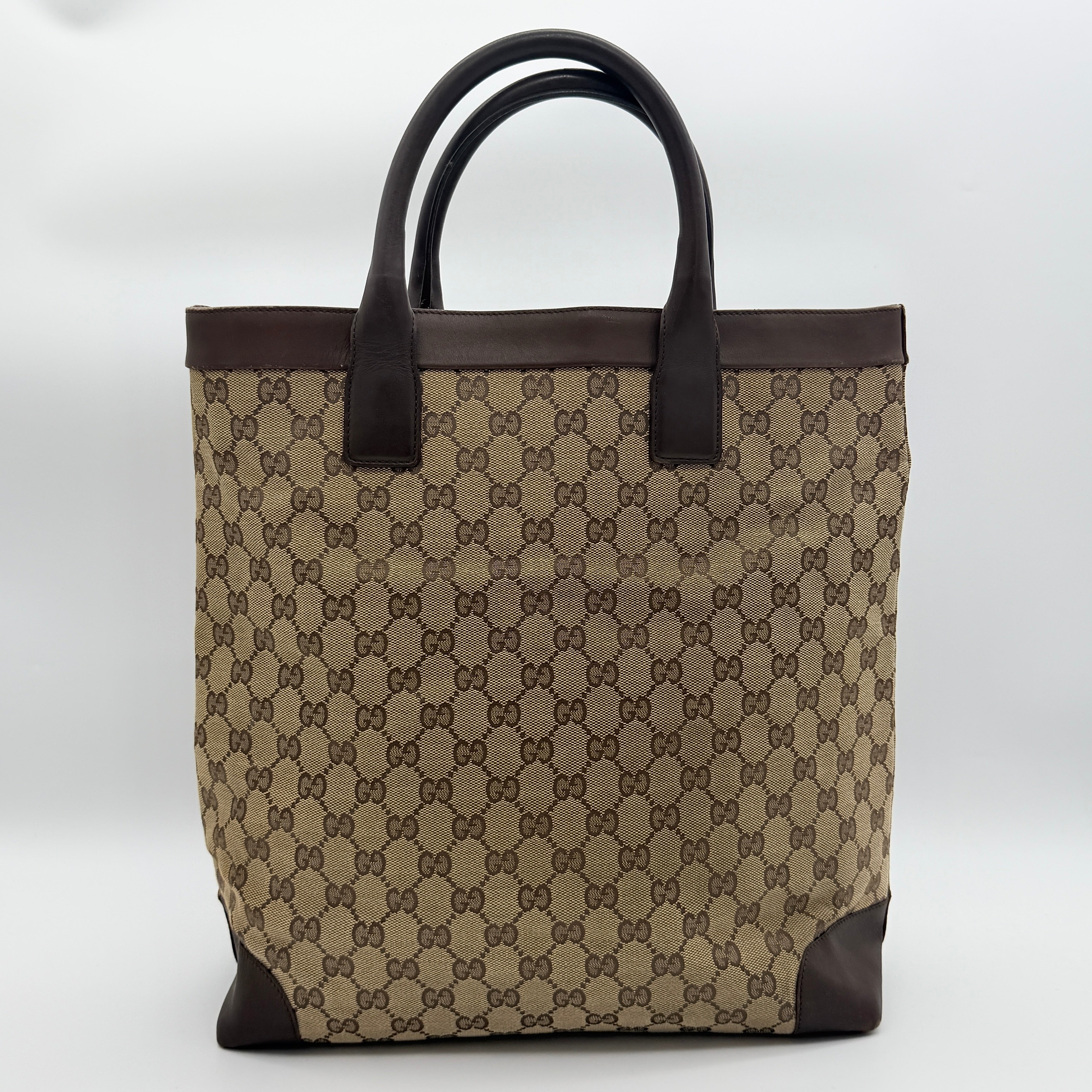 Front view of a Gucci GG Monogram Tote Bag in beige and brown canvas with dark leather trim and structured handles.