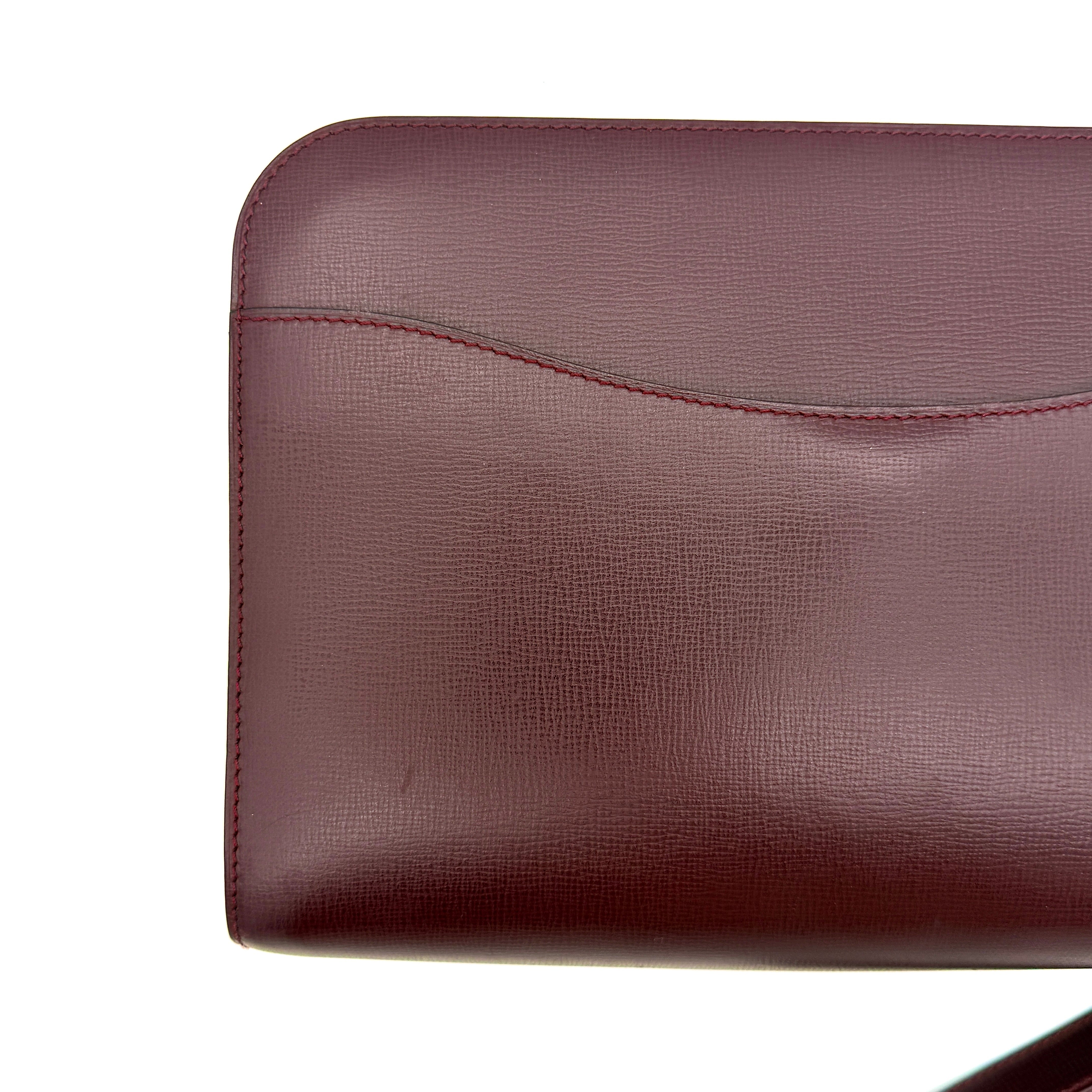 Cartier Must de Cartier clutch in burgundy leather with gold-tone zip and wrist strap, shown against a white background.