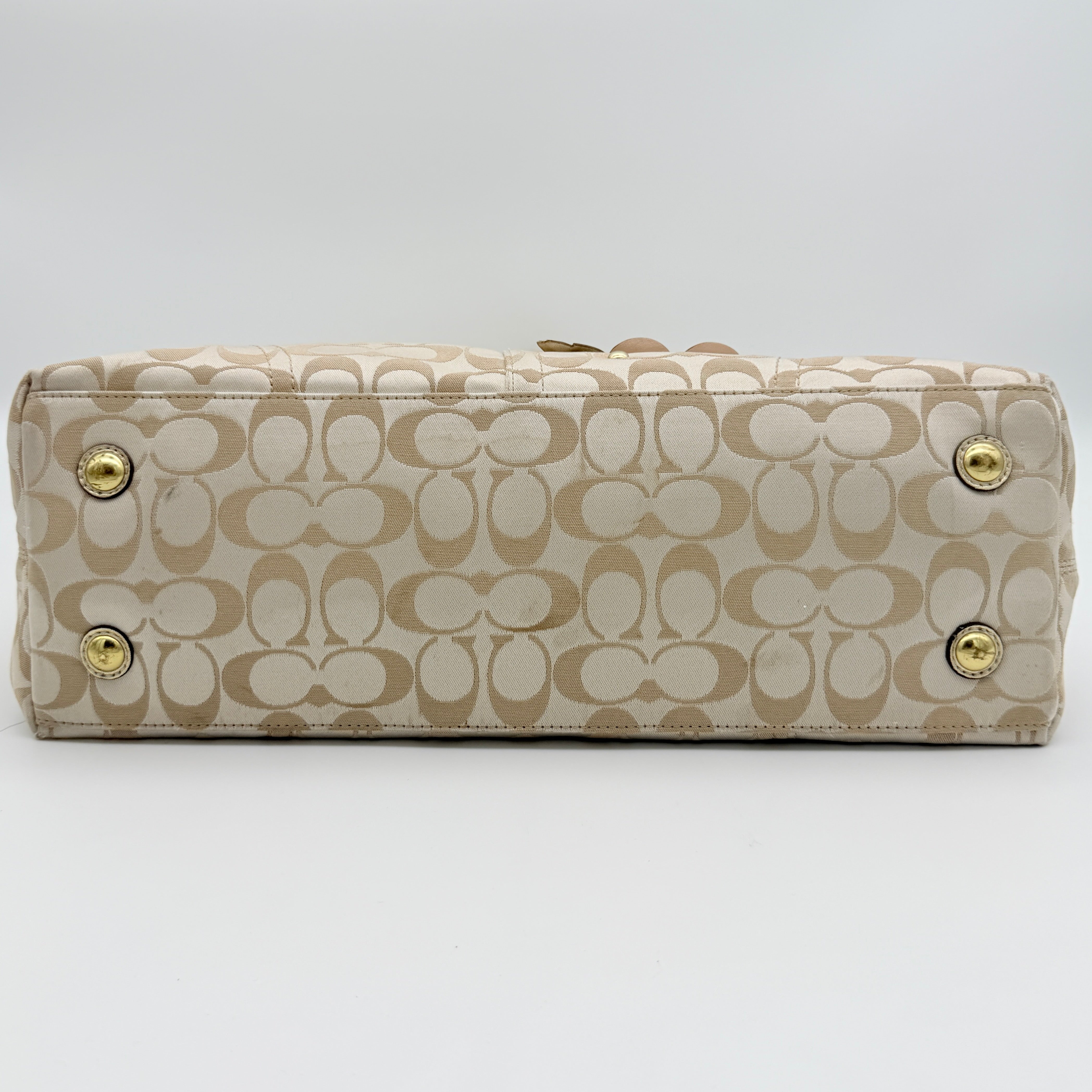 Coach beige carryall tote with floral appliqué and gold-tone handles, styled on a white background.