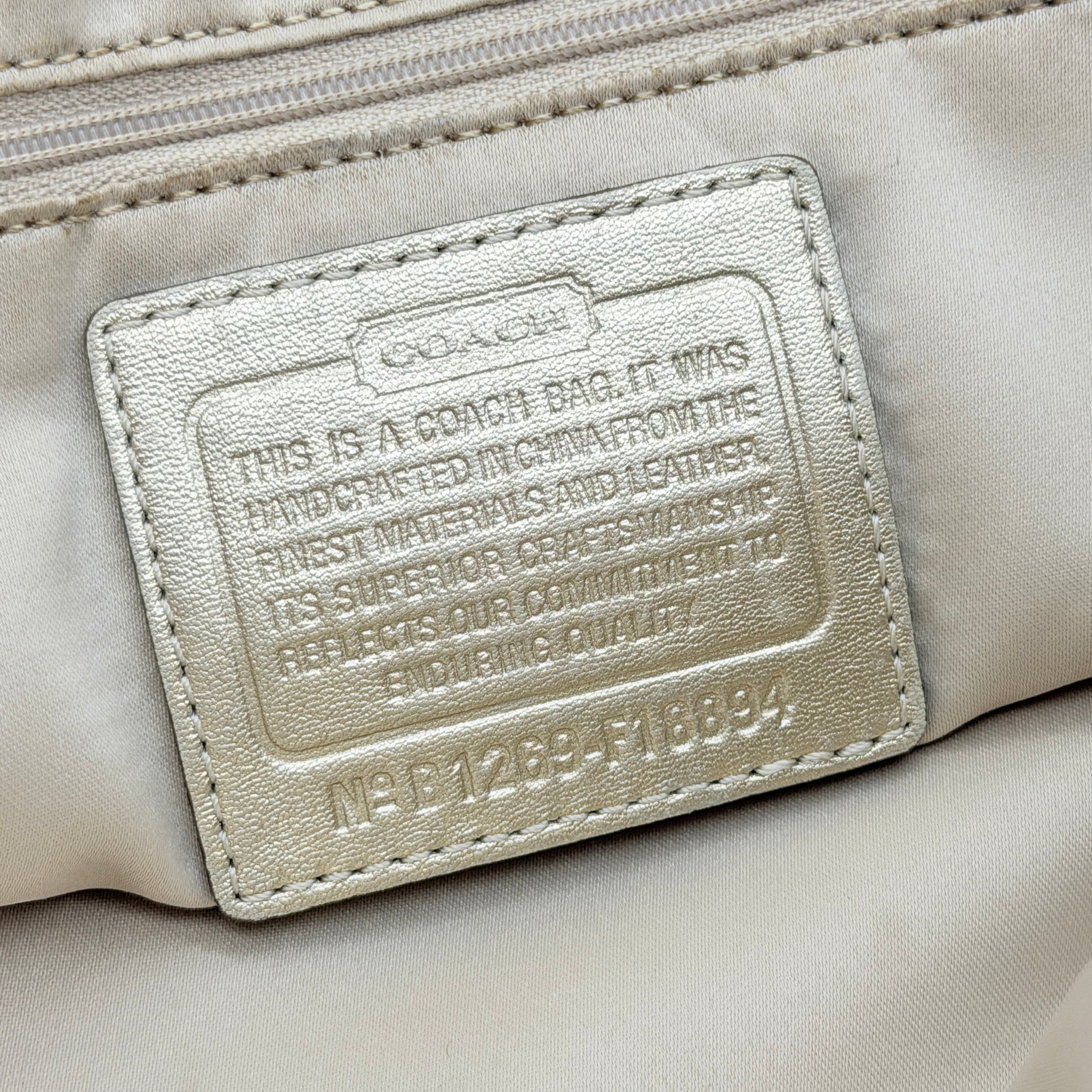 Coach beige carryall tote with floral appliqué and gold-tone handles, styled on a white background.