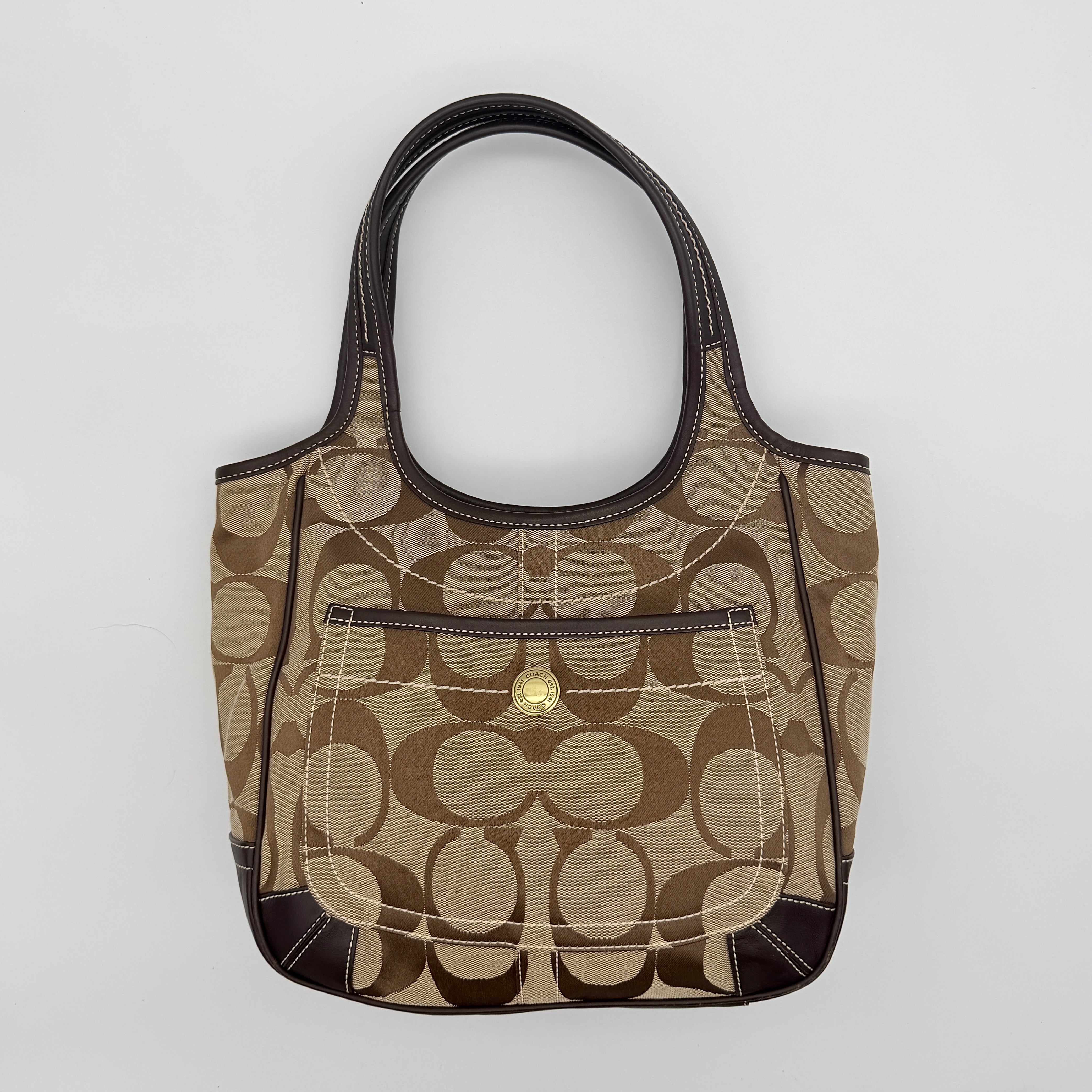 Coach Signature Ergo Hobo Tote Bag in beige and brown canvas with front pocket and dark leather trim, shown on a white background.