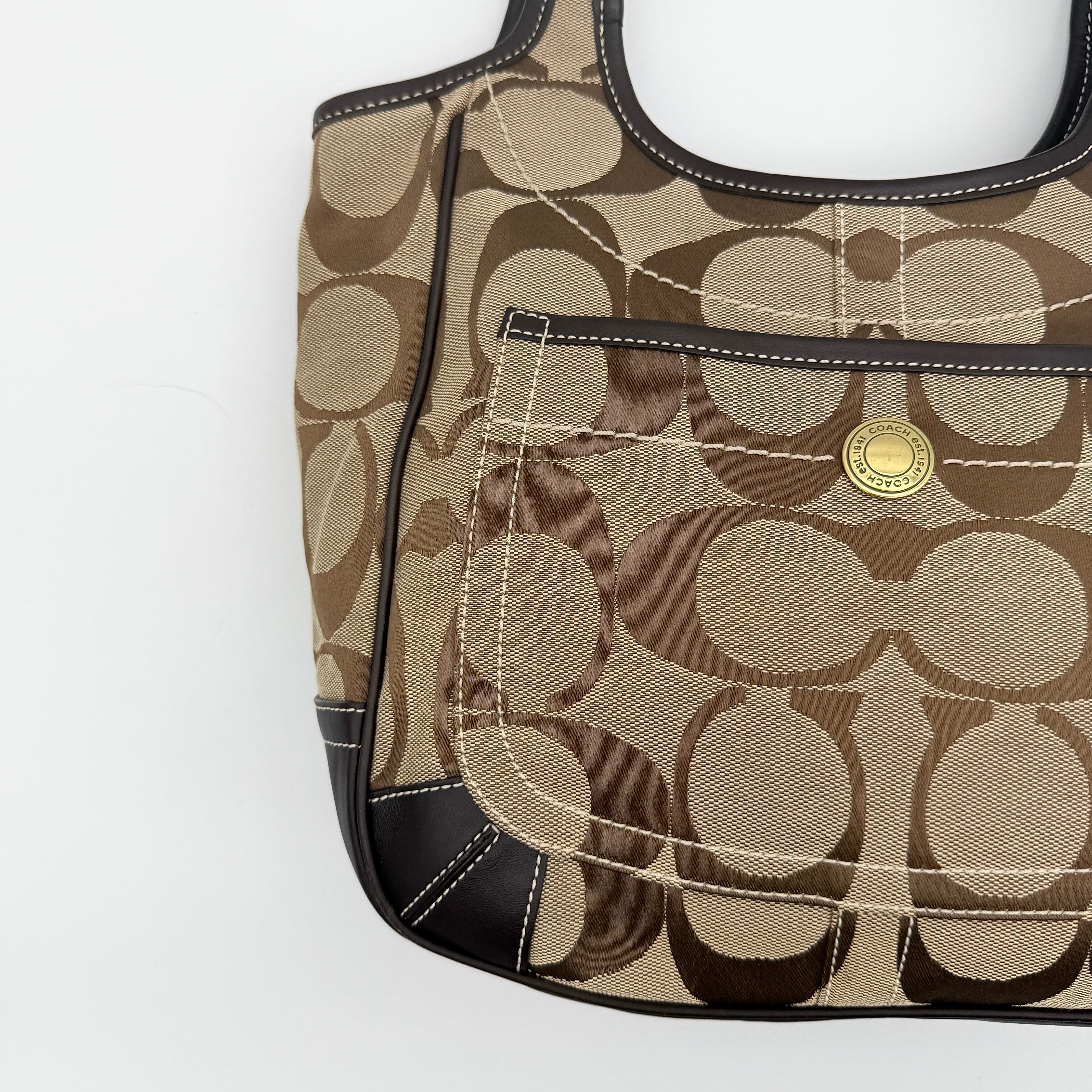 Coach Signature Ergo Hobo Tote Bag in beige and brown canvas with front pocket and dark leather trim, shown on a white background.