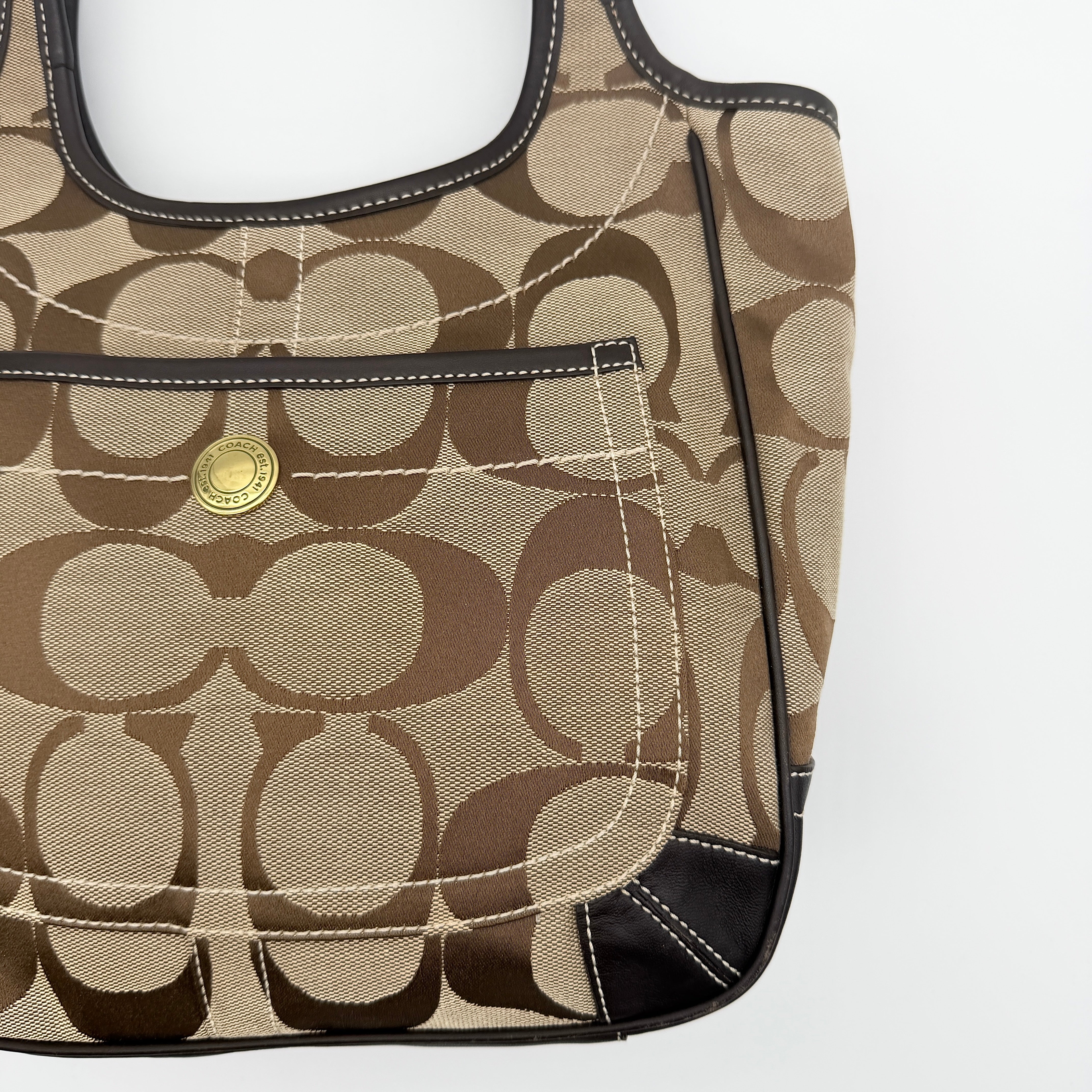 Coach Signature Ergo Hobo Tote Bag in beige and brown canvas with front pocket and dark leather trim, shown on a white background.