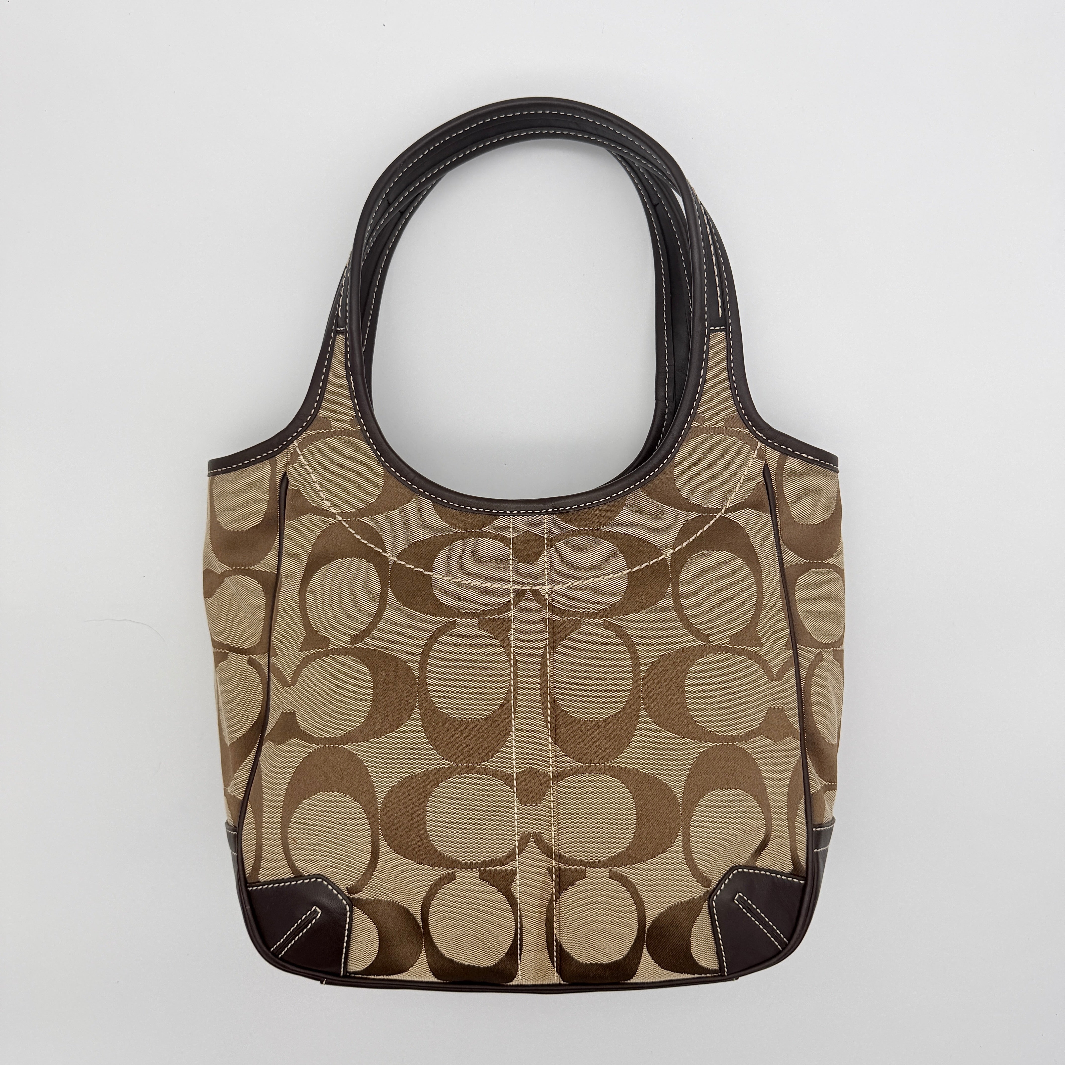Coach Signature Ergo Hobo Tote Bag in beige and brown canvas with front pocket and dark leather trim, shown on a white background.