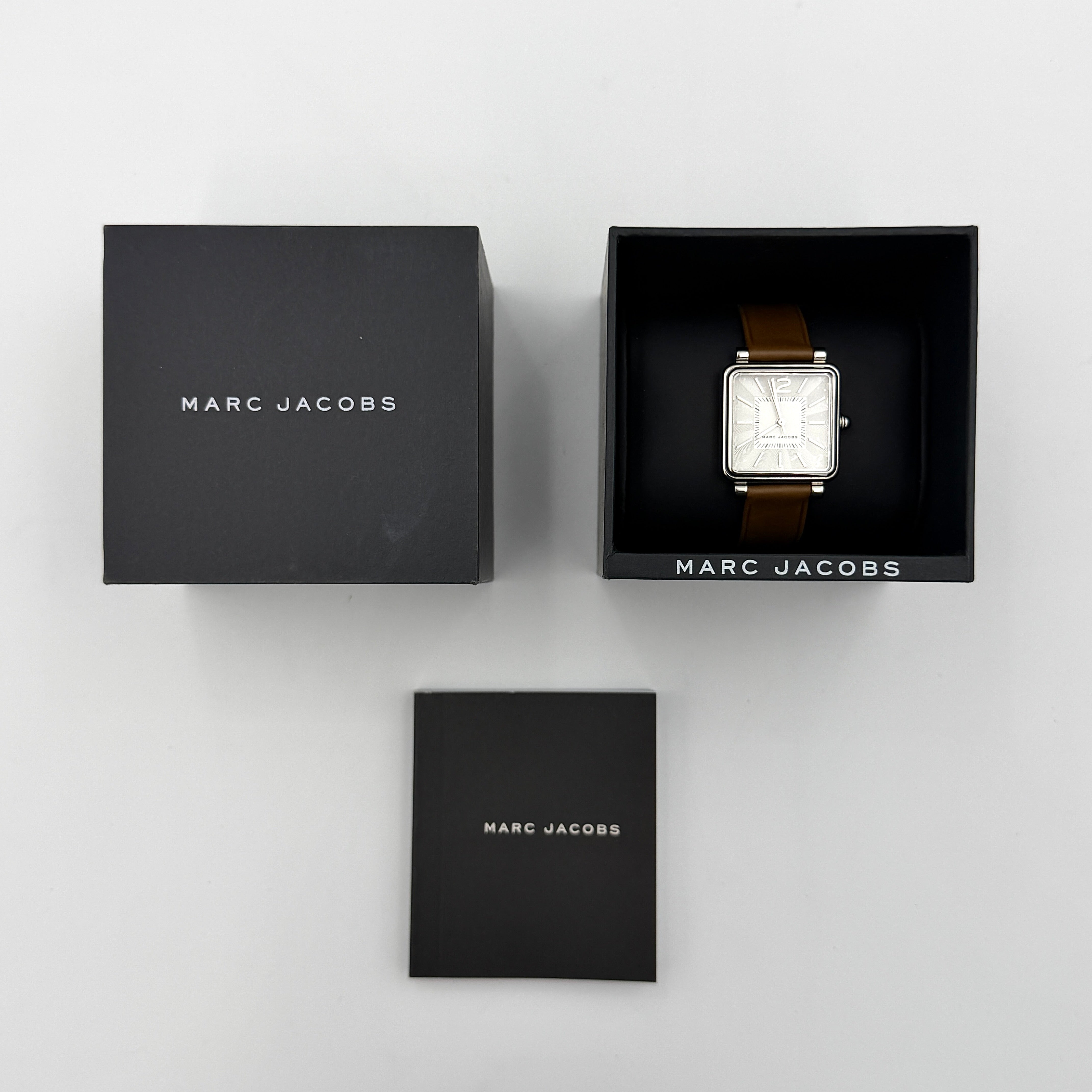 Marc Jacobs MJ1436 silver square watch with brown leather strap displayed on a branded watch cushion.