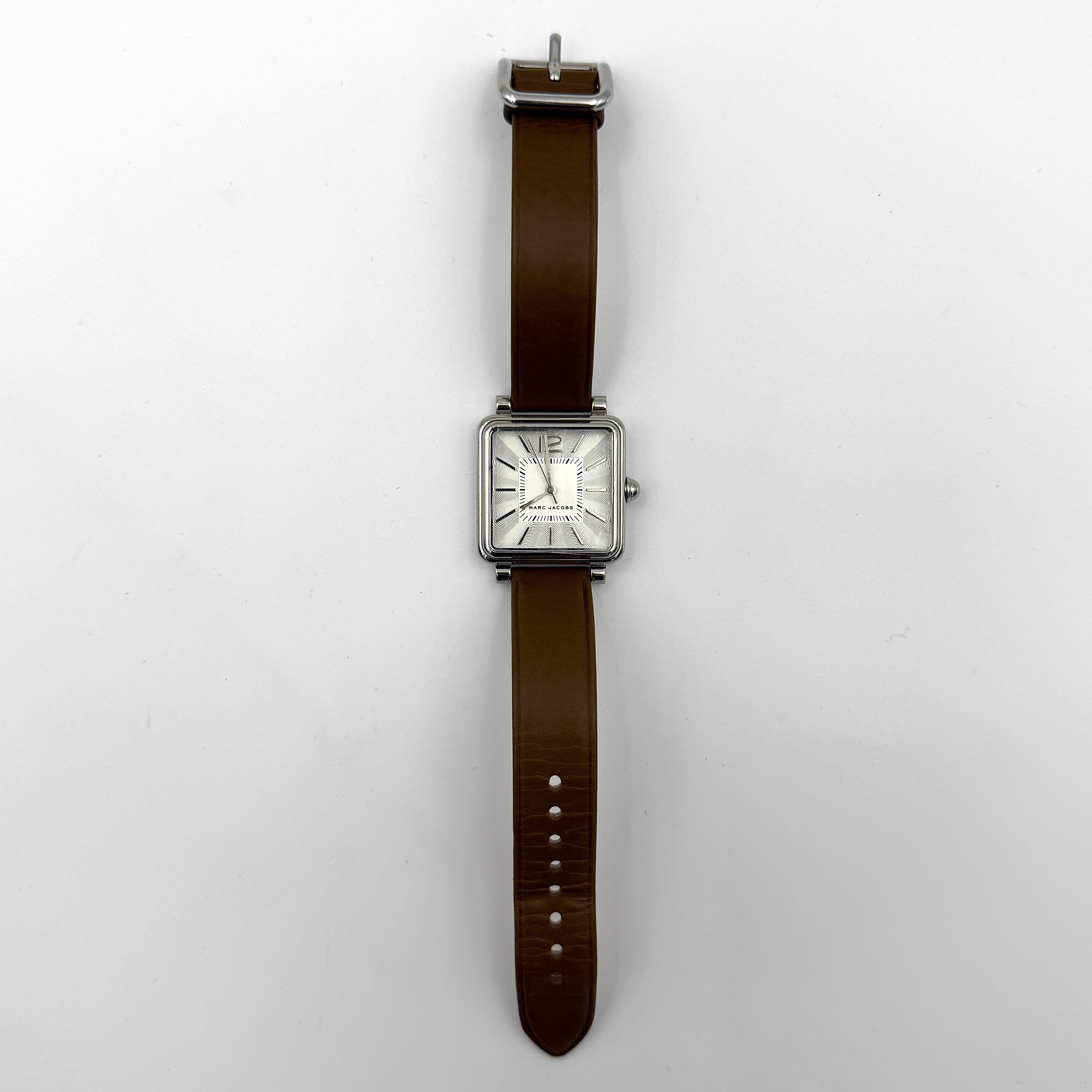 Marc Jacobs MJ1436 silver square watch with brown leather strap displayed on a branded watch cushion.
