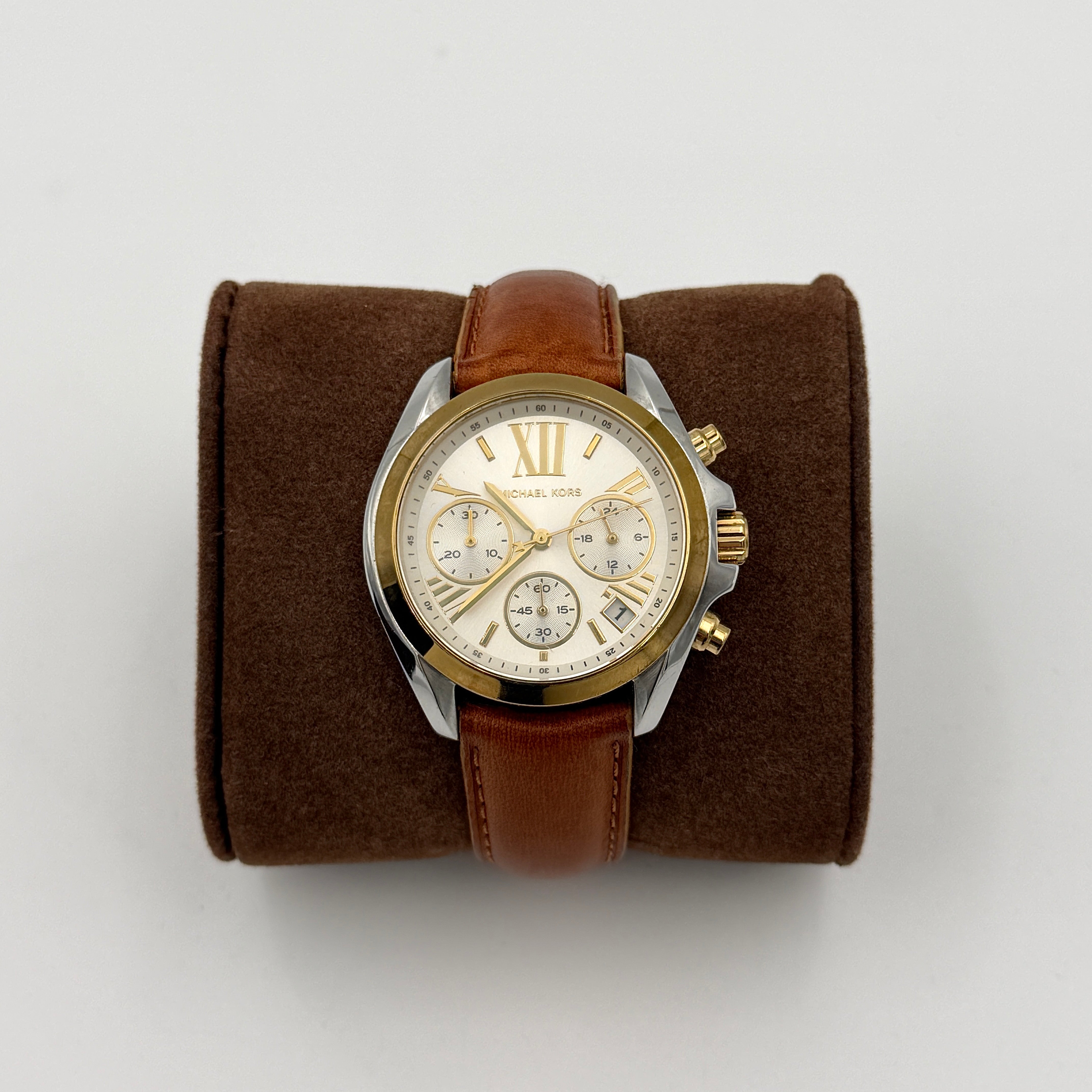 Michael Kors MK-2301 gold and silver tone chronograph watch with brown leather strap, showcased on a brown cushion atop the branded box.