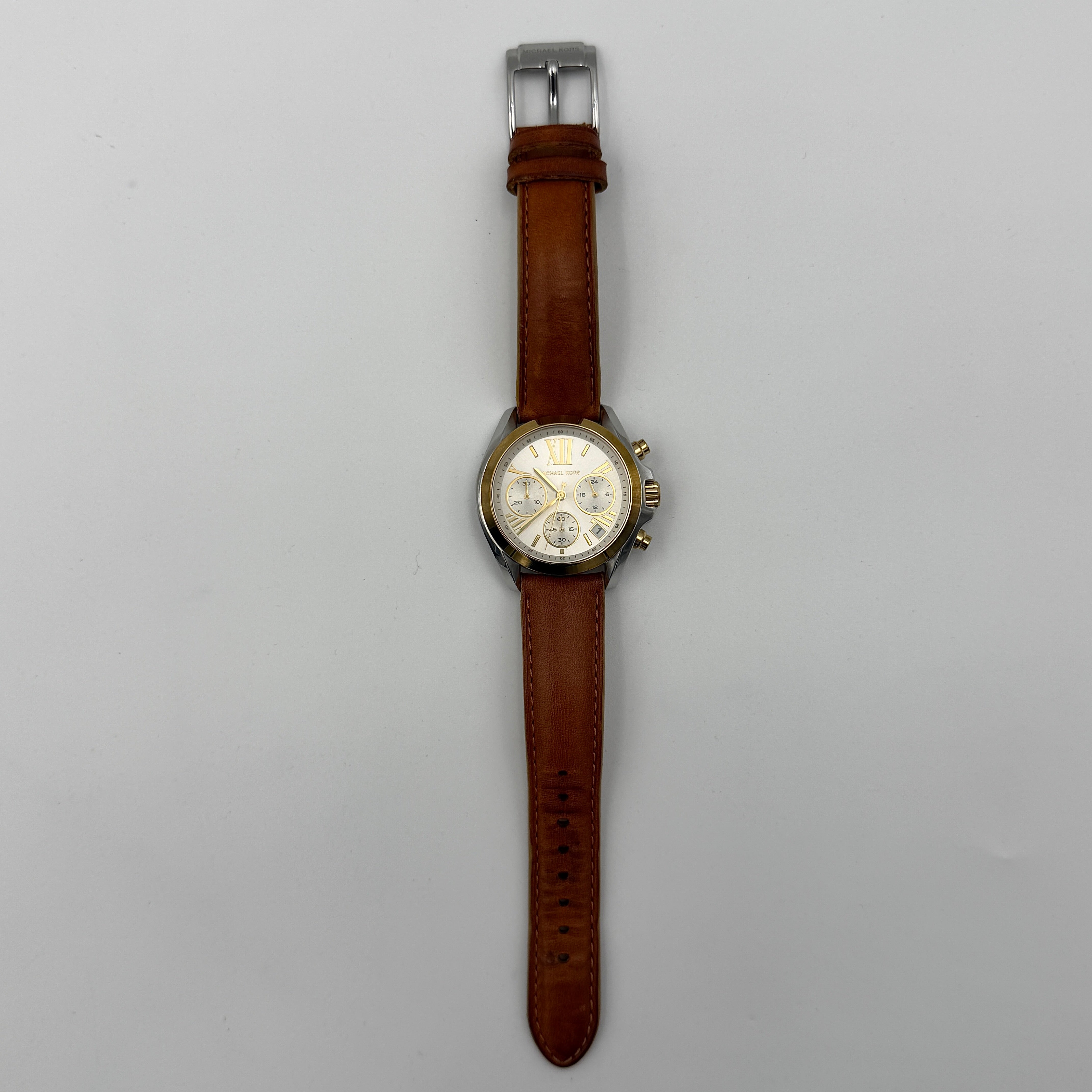 Michael Kors MK-2301 gold and silver tone chronograph watch with brown leather strap, showcased on a brown cushion atop the branded box.