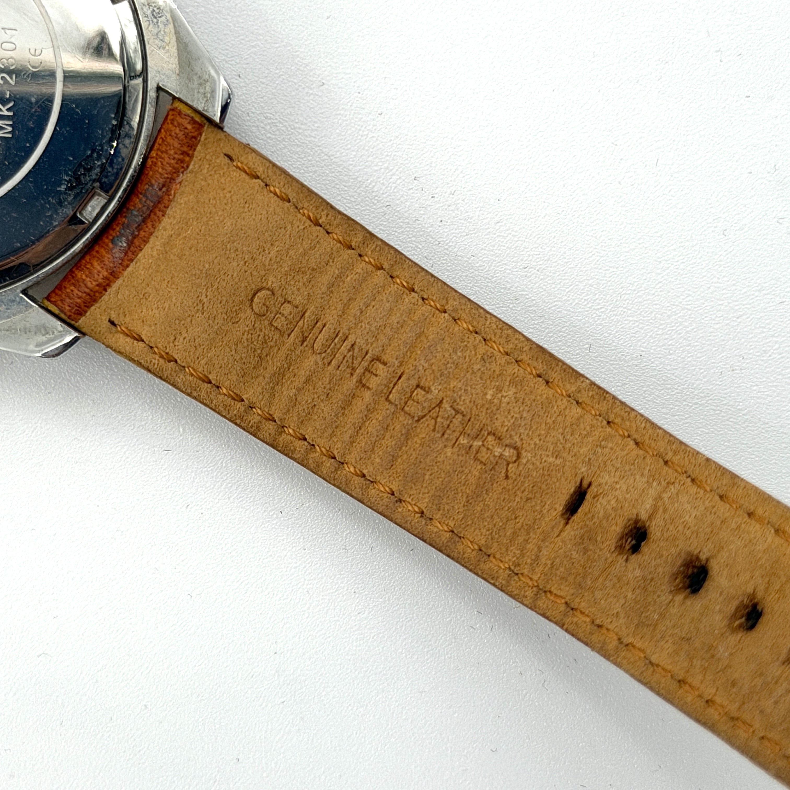 Michael Kors MK-2301 gold and silver tone chronograph watch with brown leather strap, showcased on a brown cushion atop the branded box.