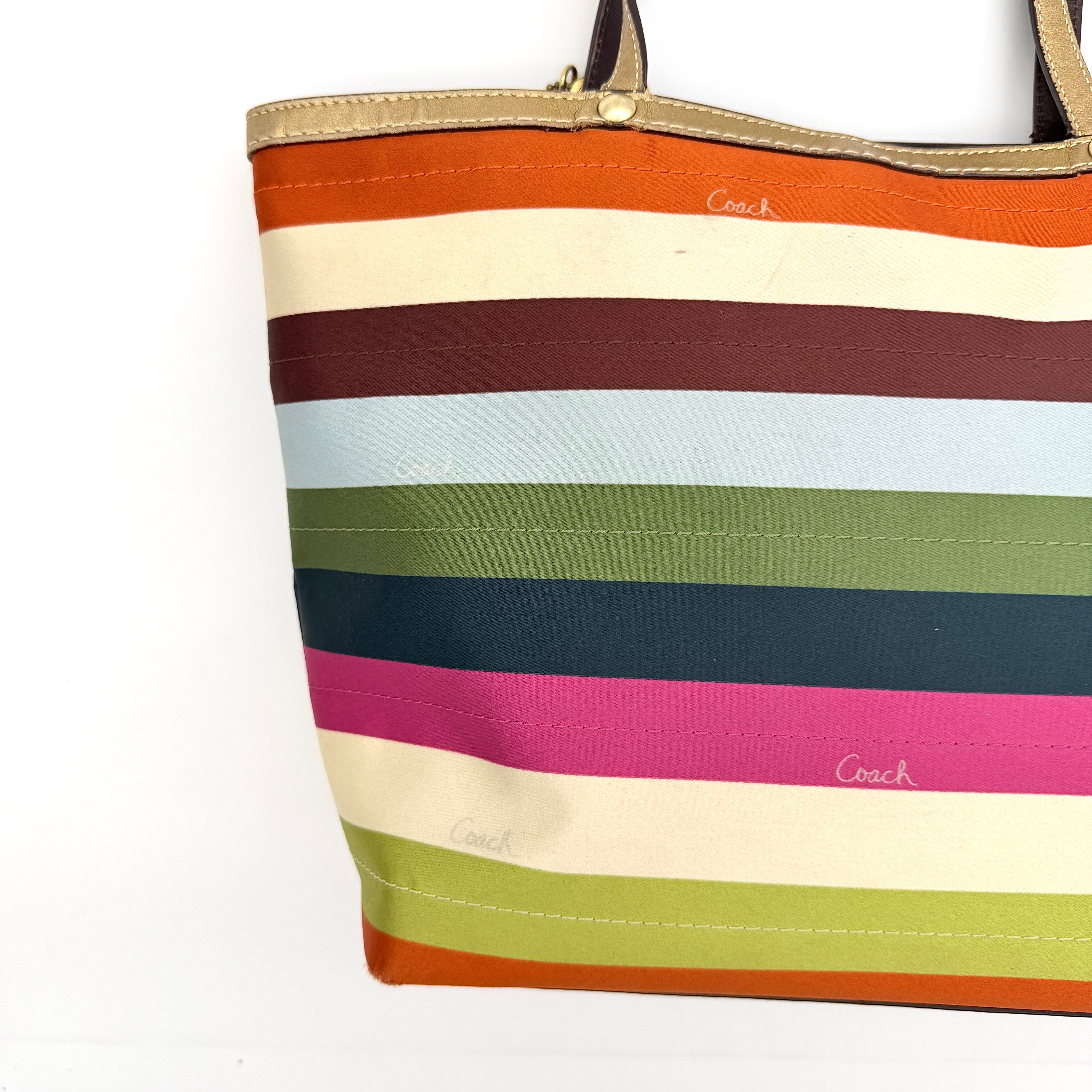Coach Legacy Stripe Tote Bag in multicolour stripes with gold leather trim and double handles, displayed against a white background.