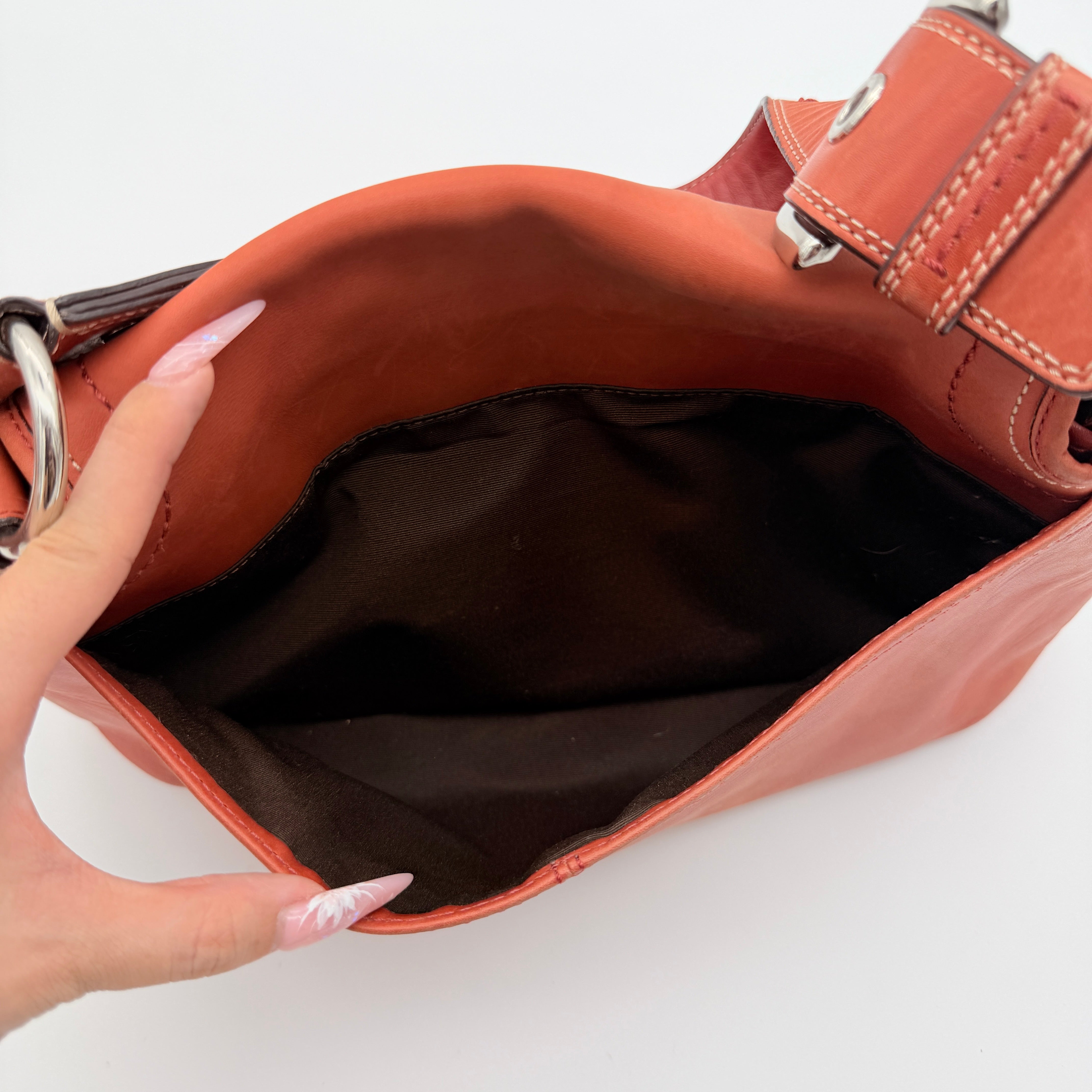 Coach Soho bag in burnt orange leather with pleated detailing and wide shoulder strap, shown on a white background.
