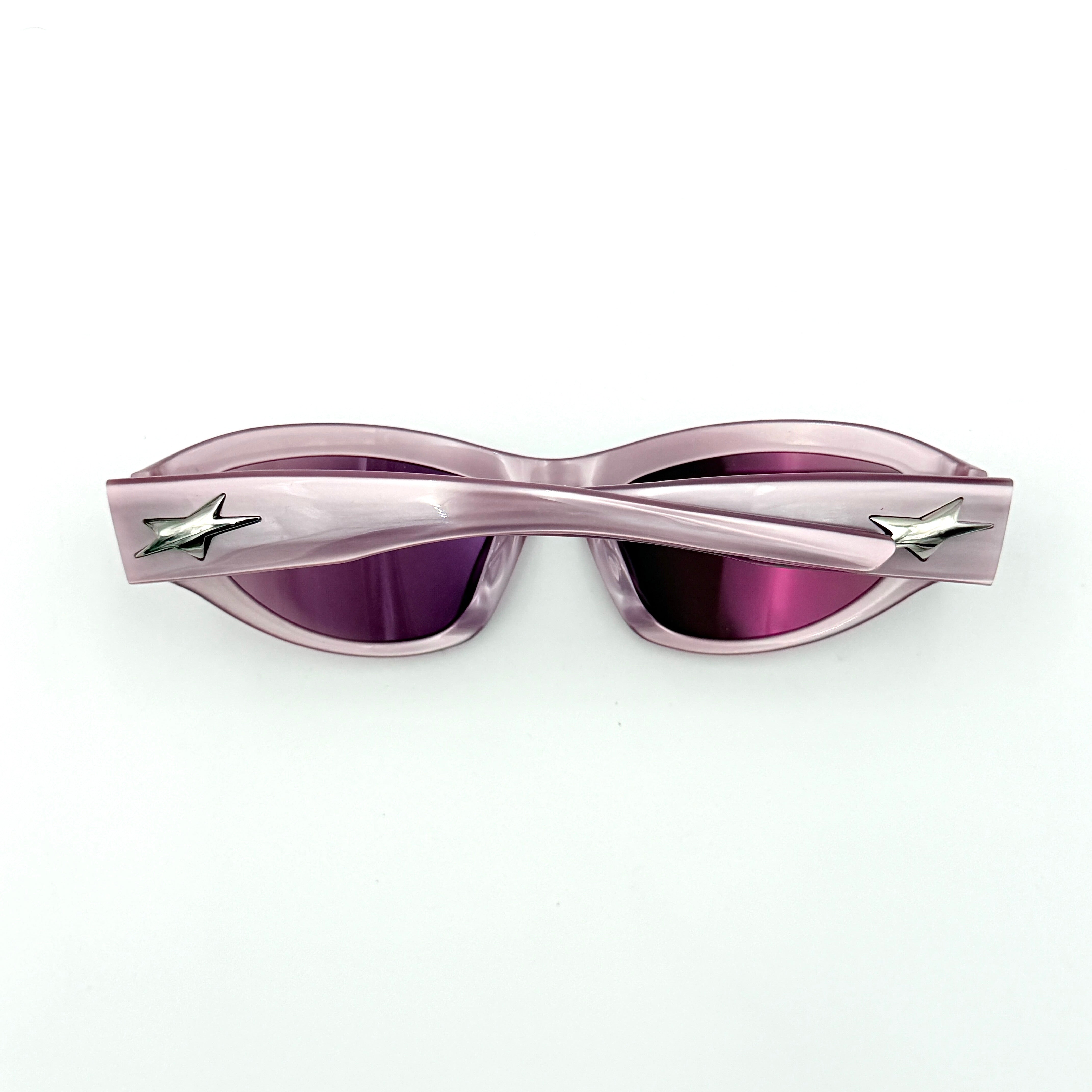 Gentle Monster R.E.A.T sunglasses in translucent pink acetate with mirrored pink lenses and silver star hardware, displayed alongside a chrome hard case.