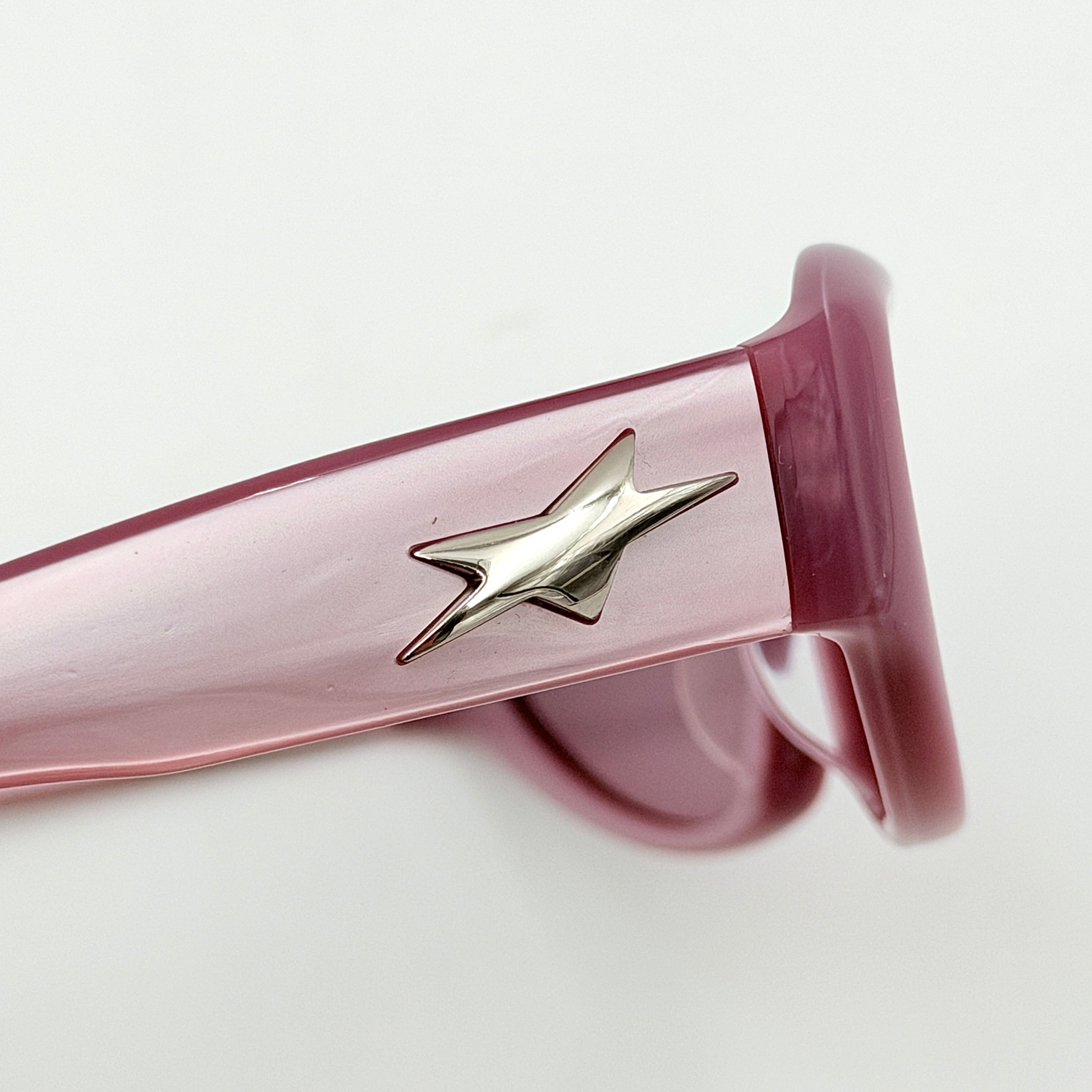 Gentle Monster R.E.A.T sunglasses in translucent pink acetate with mirrored pink lenses and silver star hardware, displayed alongside a chrome hard case.