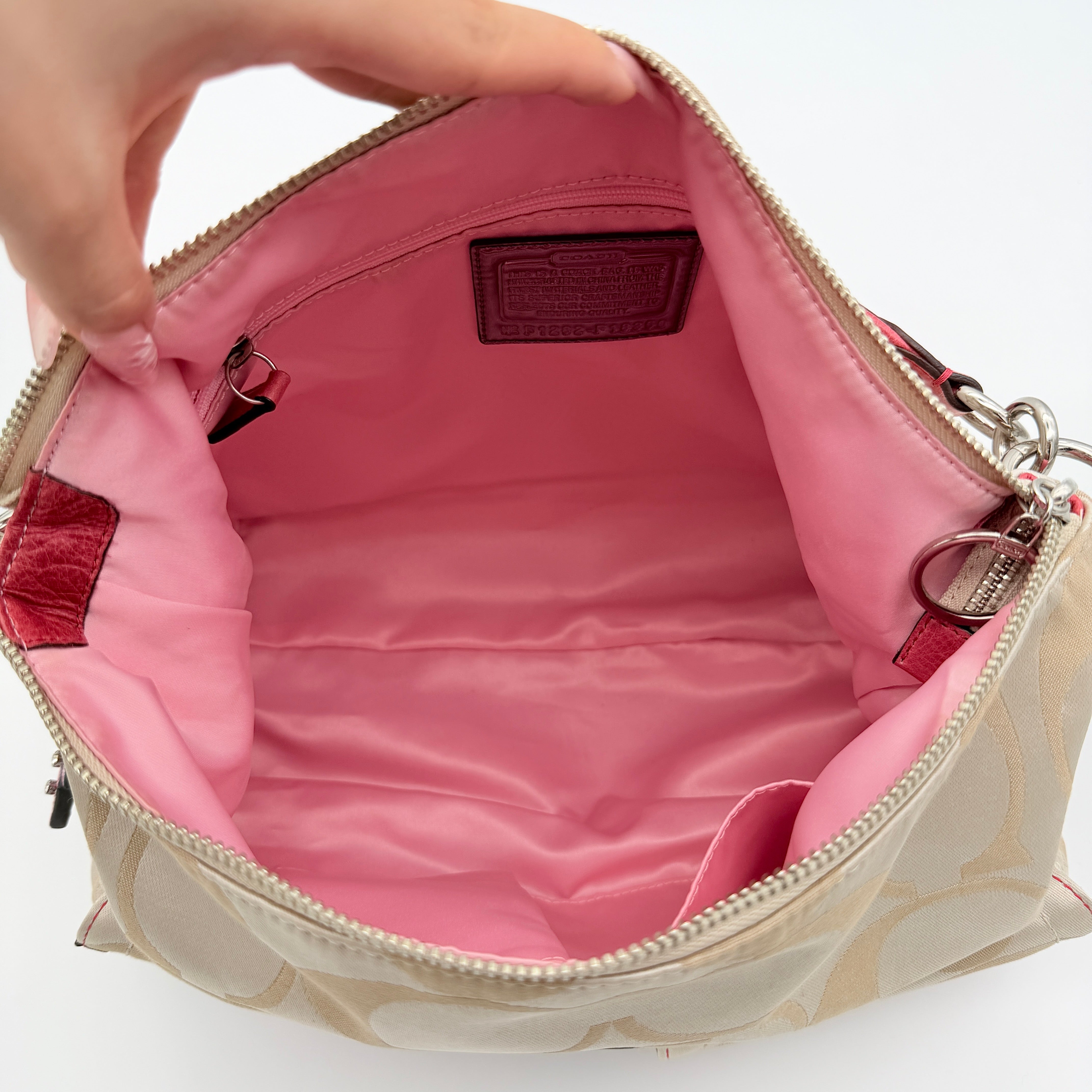 Coach Signature Poppy Pocket Hobo in beige sateen canvas with pink leather trim and silver hardware, front view with double pockets and charms.
