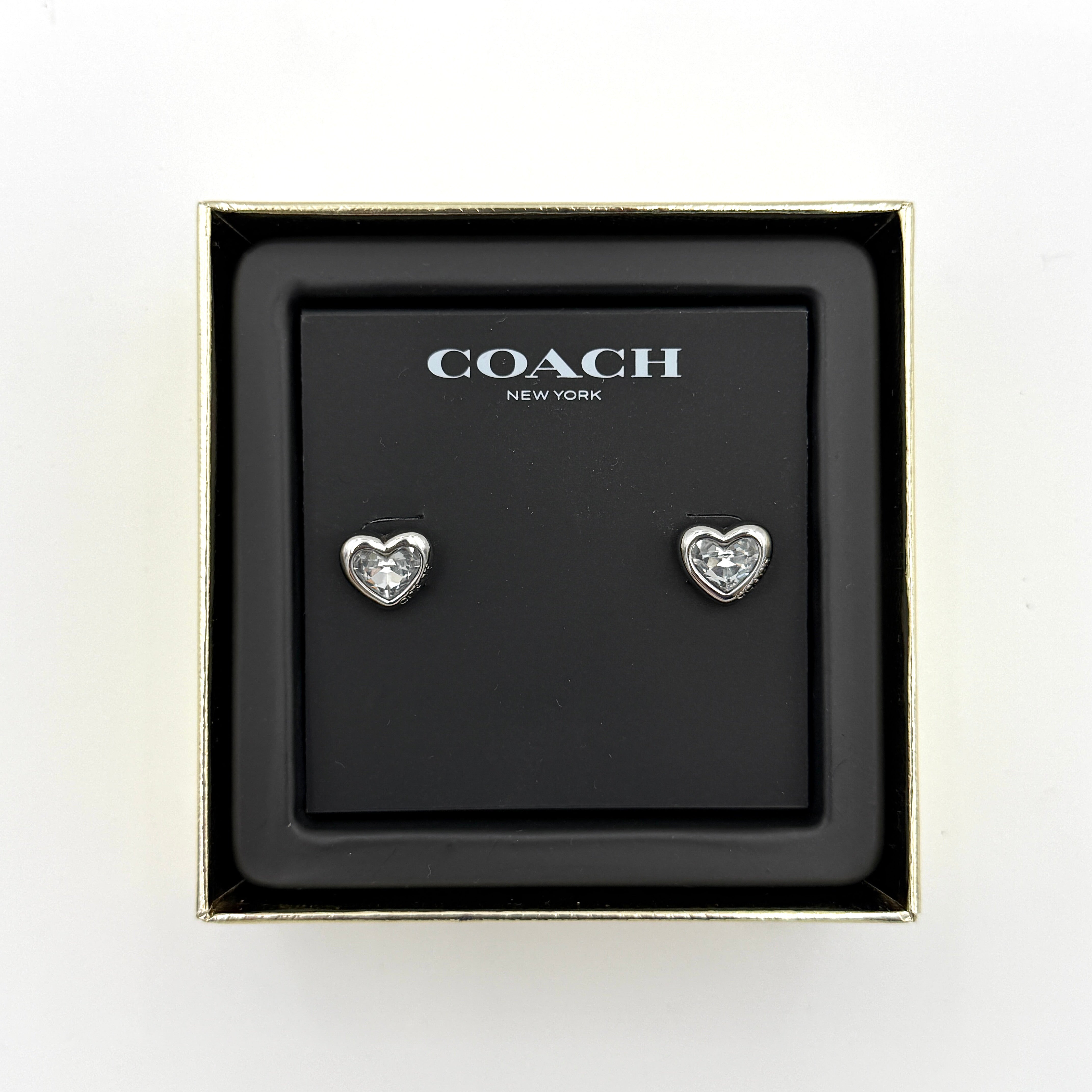 A pair of Coach heart-shaped crystal stud earrings in silver-tone metal with engraved logo and faceted stones.
