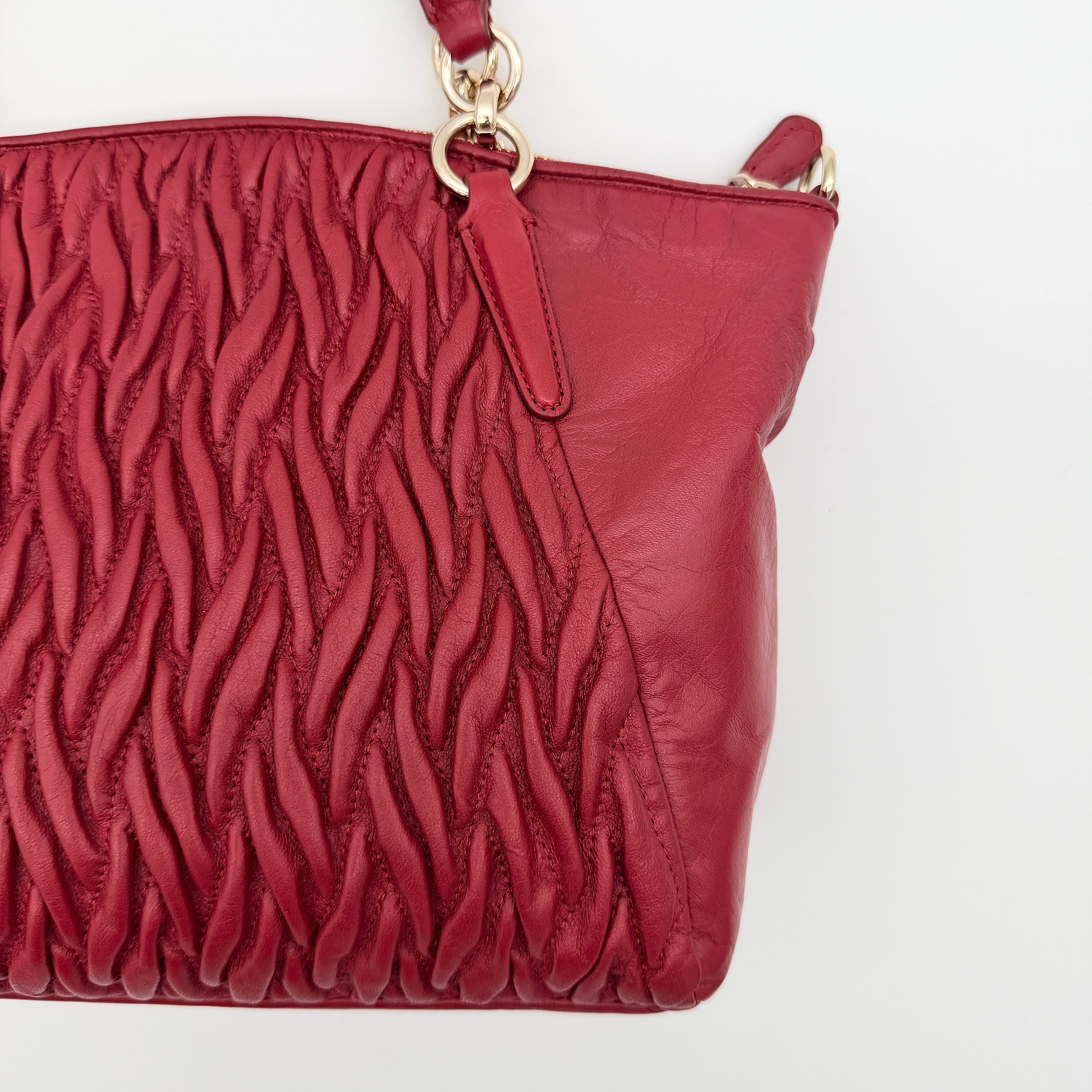 Coach Kelsey 2Way satchel in quilted red leather with gold-tone hardware and detachable strap, displayed against a white background.