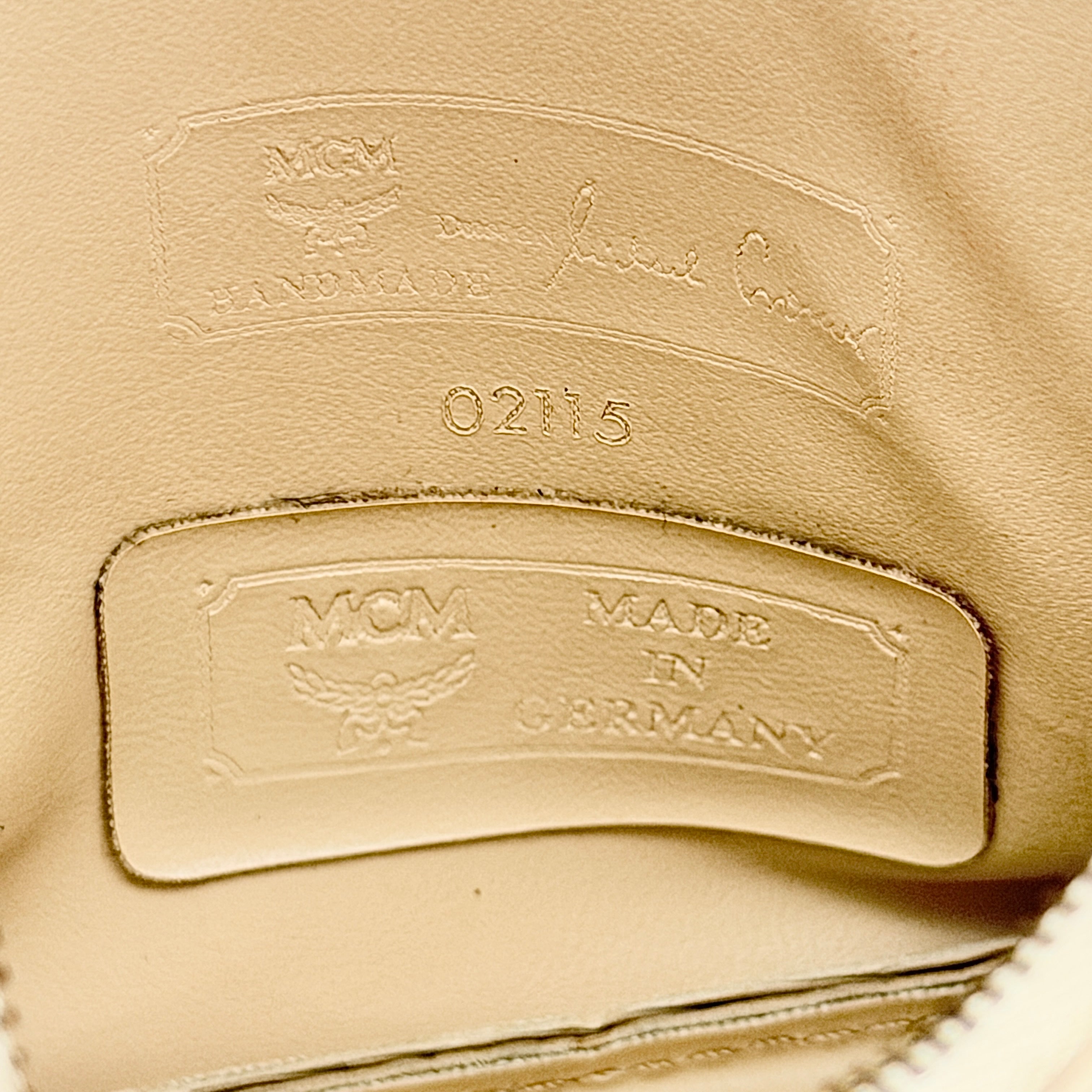 MCM beige embossed leather pouch with iconic gold logo plaque and zip closure, styled against a white background.