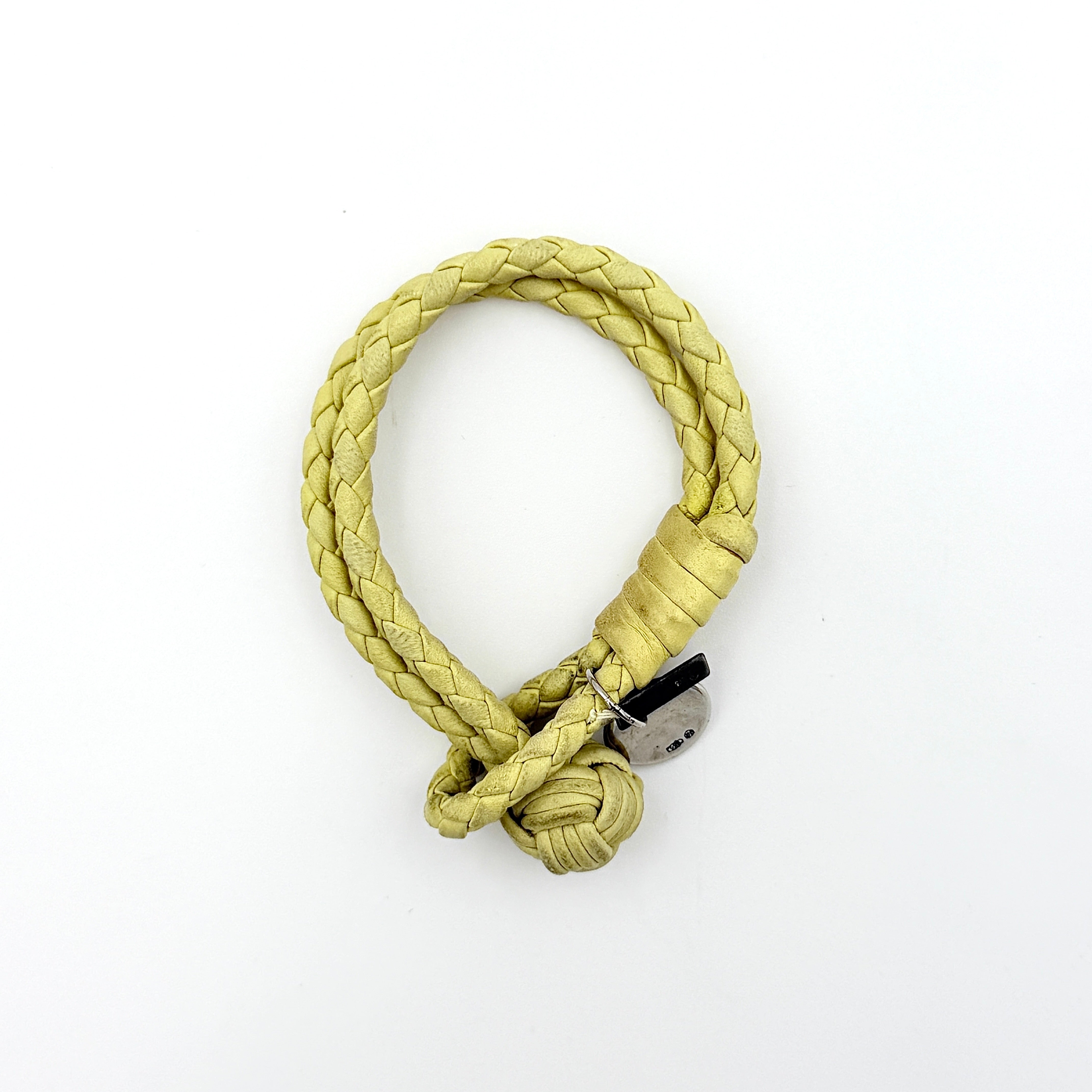 A braided pastel yellow Bottega Veneta Intrecciato leather bracelet with signature knot closure and engraved silver-tone tags.
