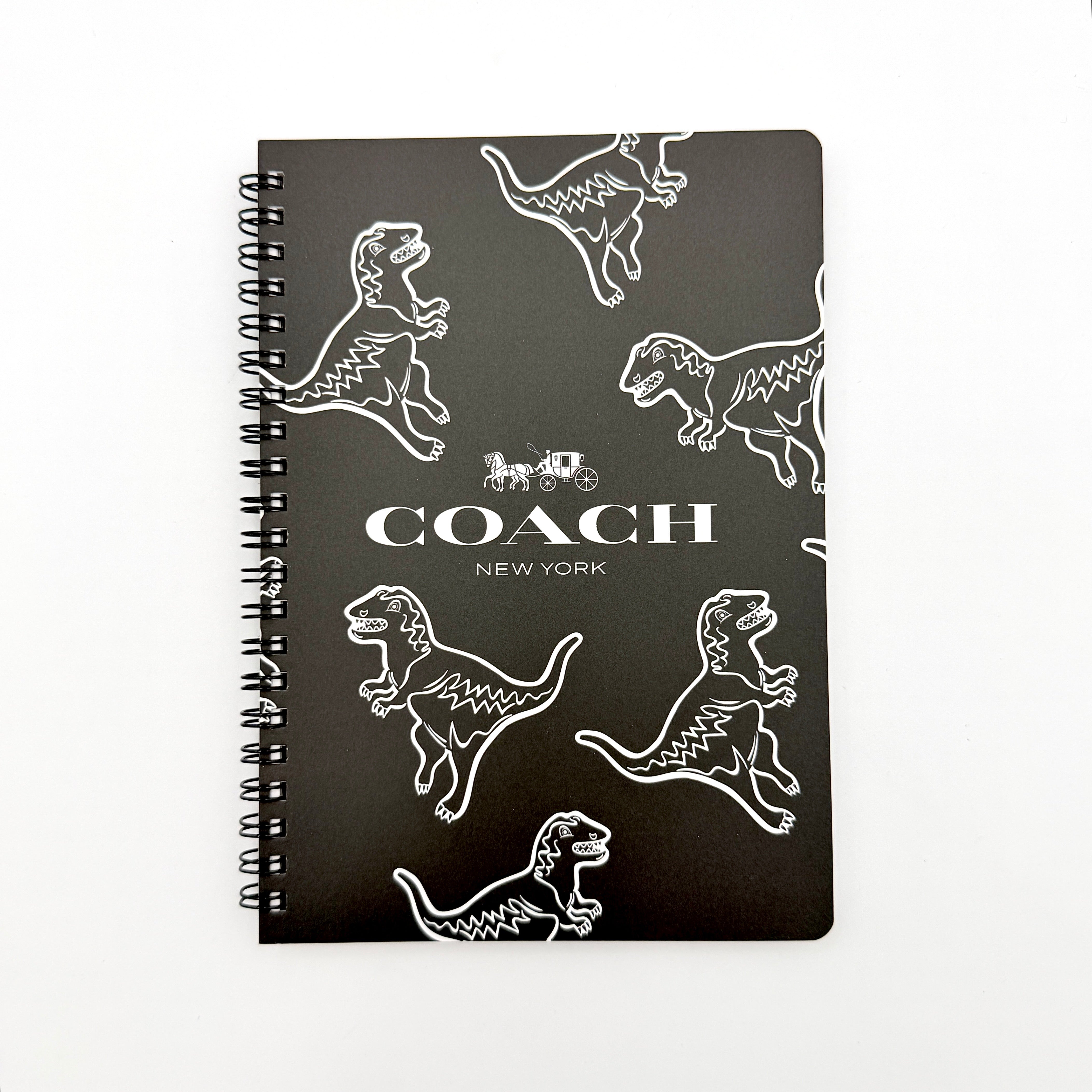 Coach Rexy Journal Notebook in black featuring white Rexy dinosaur illustrations and a spiral binding.