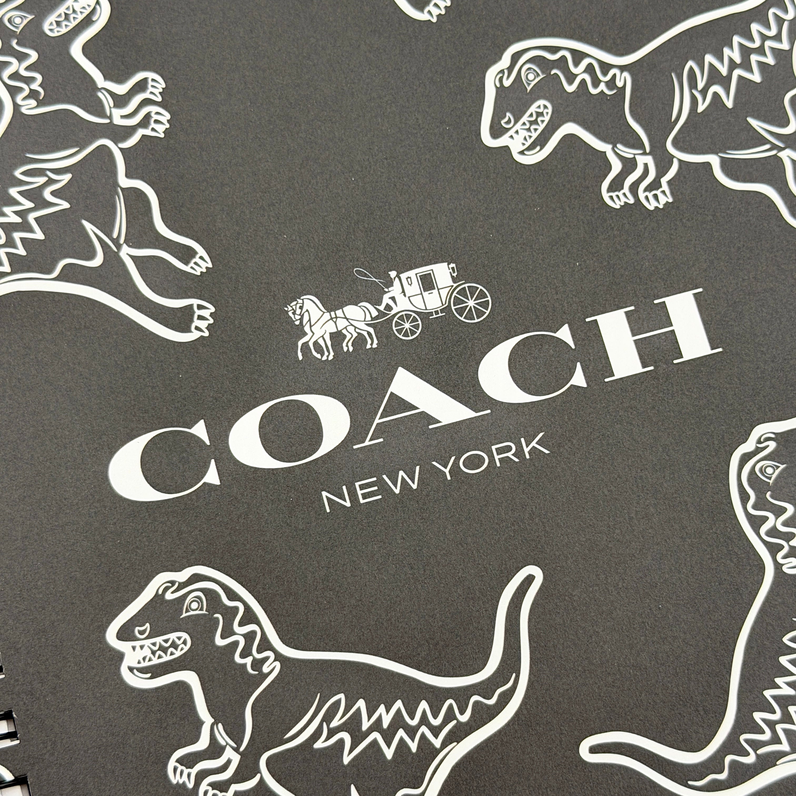 Coach Rexy Journal Notebook in black featuring white Rexy dinosaur illustrations and a spiral binding.