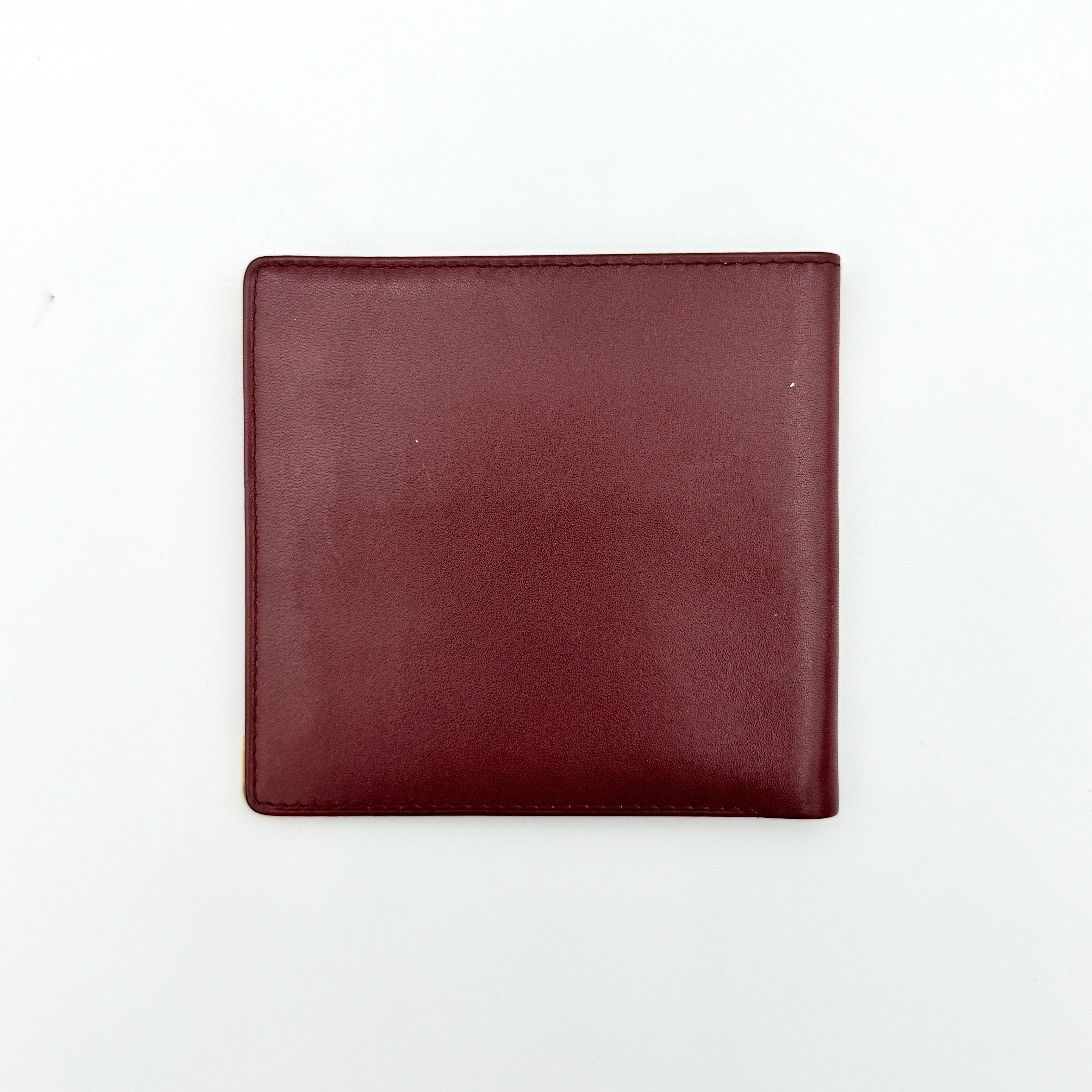 Cartier Must de Cartier leather wallet in rich burgundy with gold-tone corner accents and an embossed logo, photographed closed against a white background.