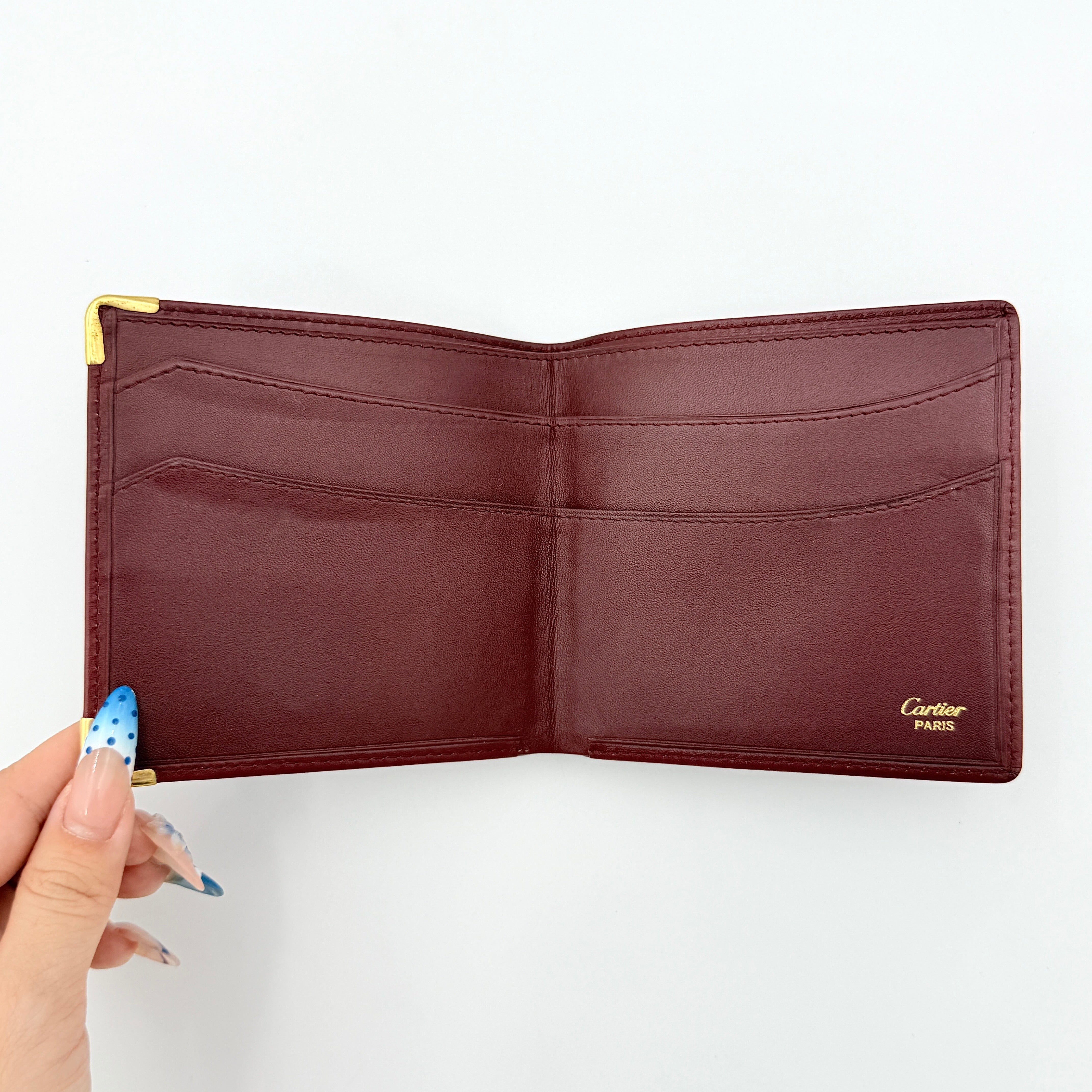 Cartier Must de Cartier leather wallet in rich burgundy with gold-tone corner accents and an embossed logo, photographed closed against a white background.