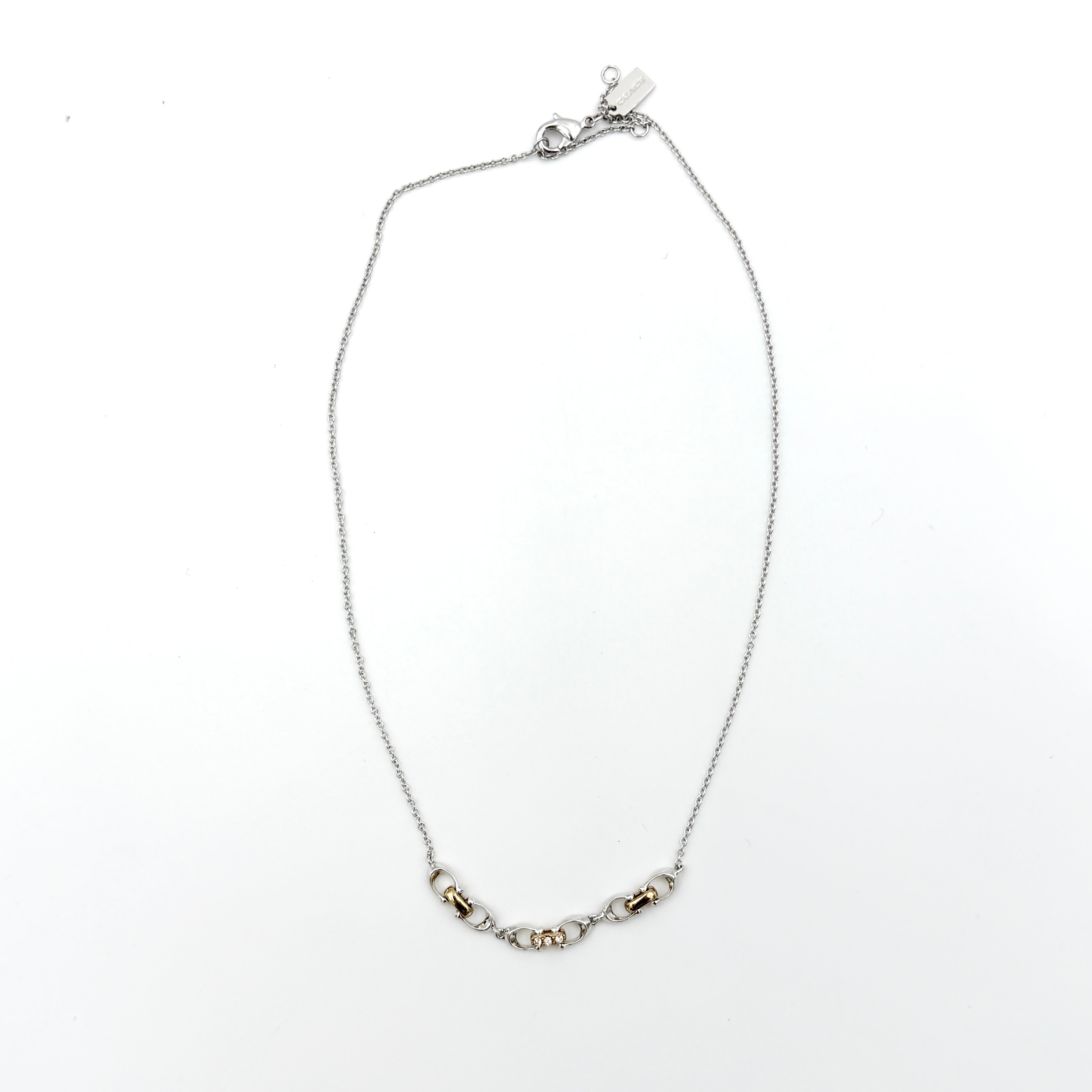 Coach Signature Linked Necklace in silver and gold tones featuring sculptural mixed-metal links and a central crystal accent.