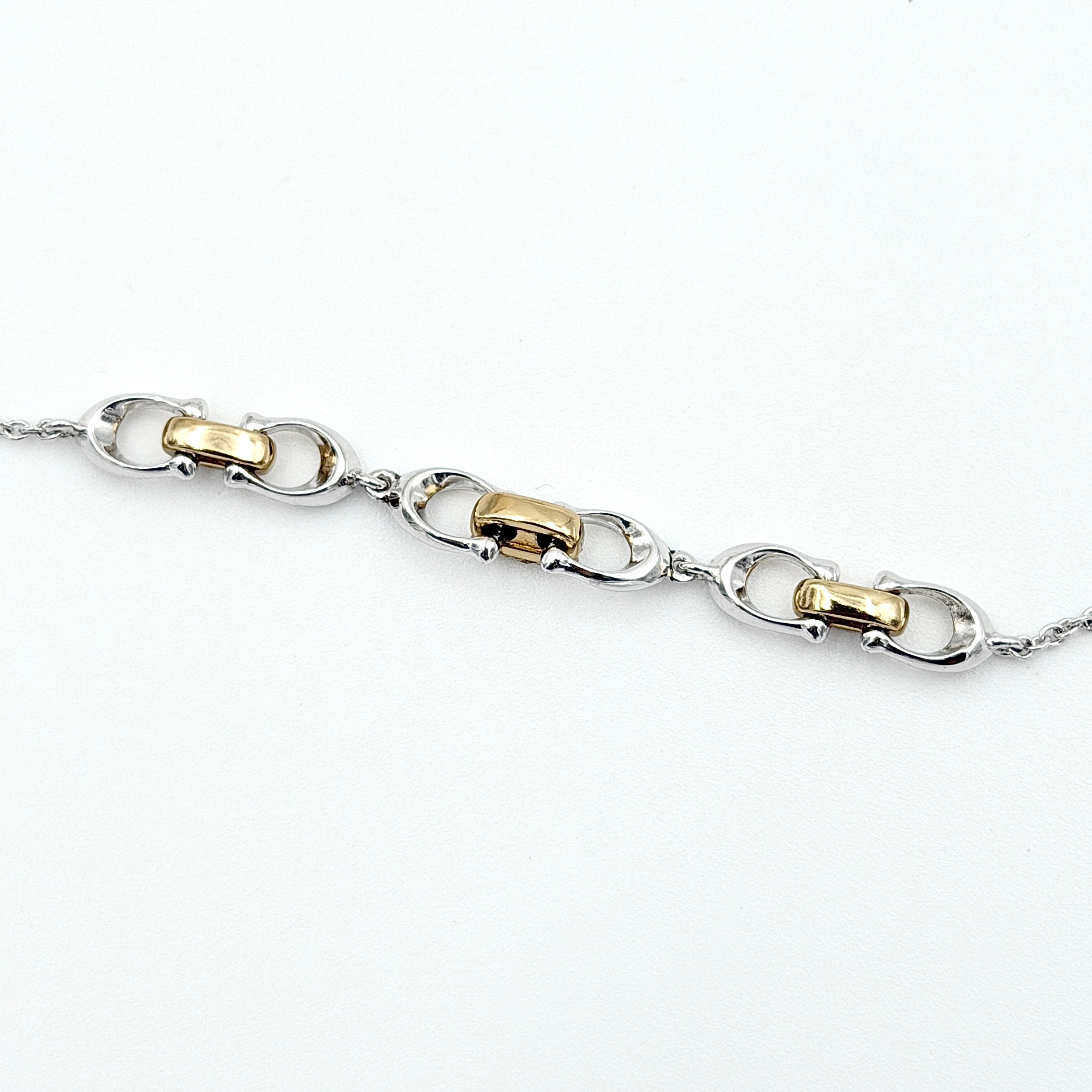 Coach Signature Linked Necklace in silver and gold tones featuring sculptural mixed-metal links and a central crystal accent.