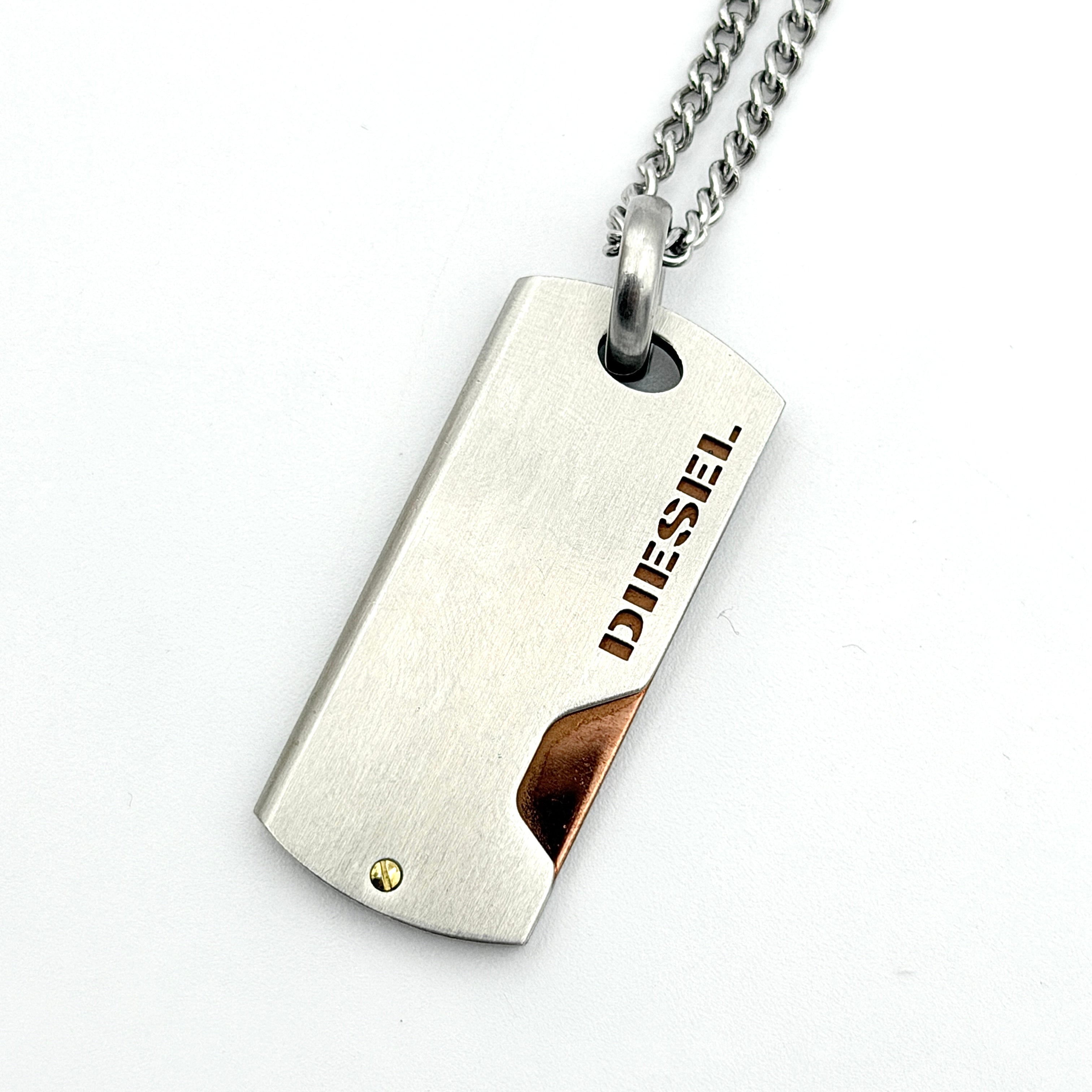 Diesel silver-tone stainless steel dog tag necklace with bronze accent, curb chain, and round detail showcased on a white background.