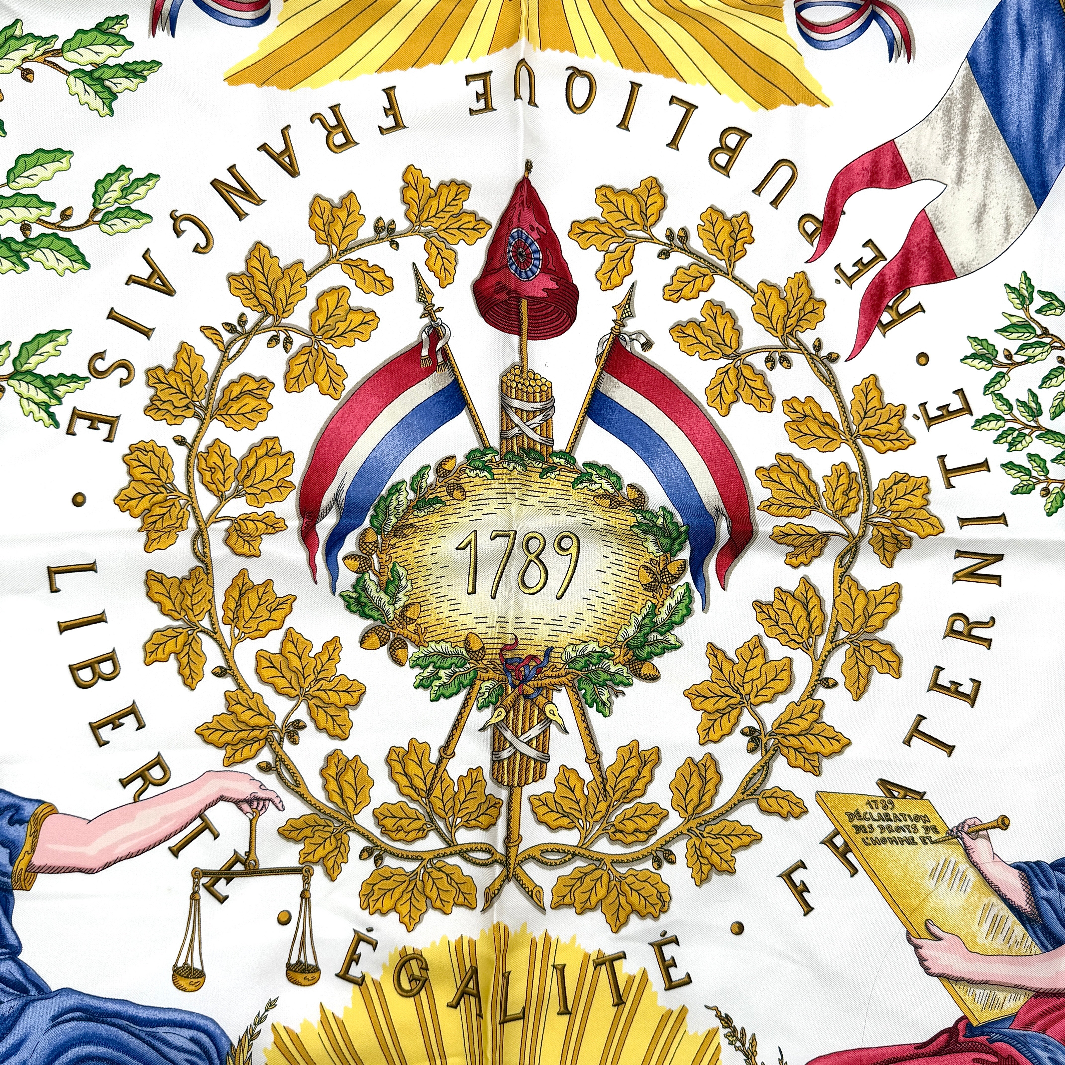 Hermès silk scarf with blue border, featuring a detailed French revolutionary motif and classical figures, shown with its signature orange box.