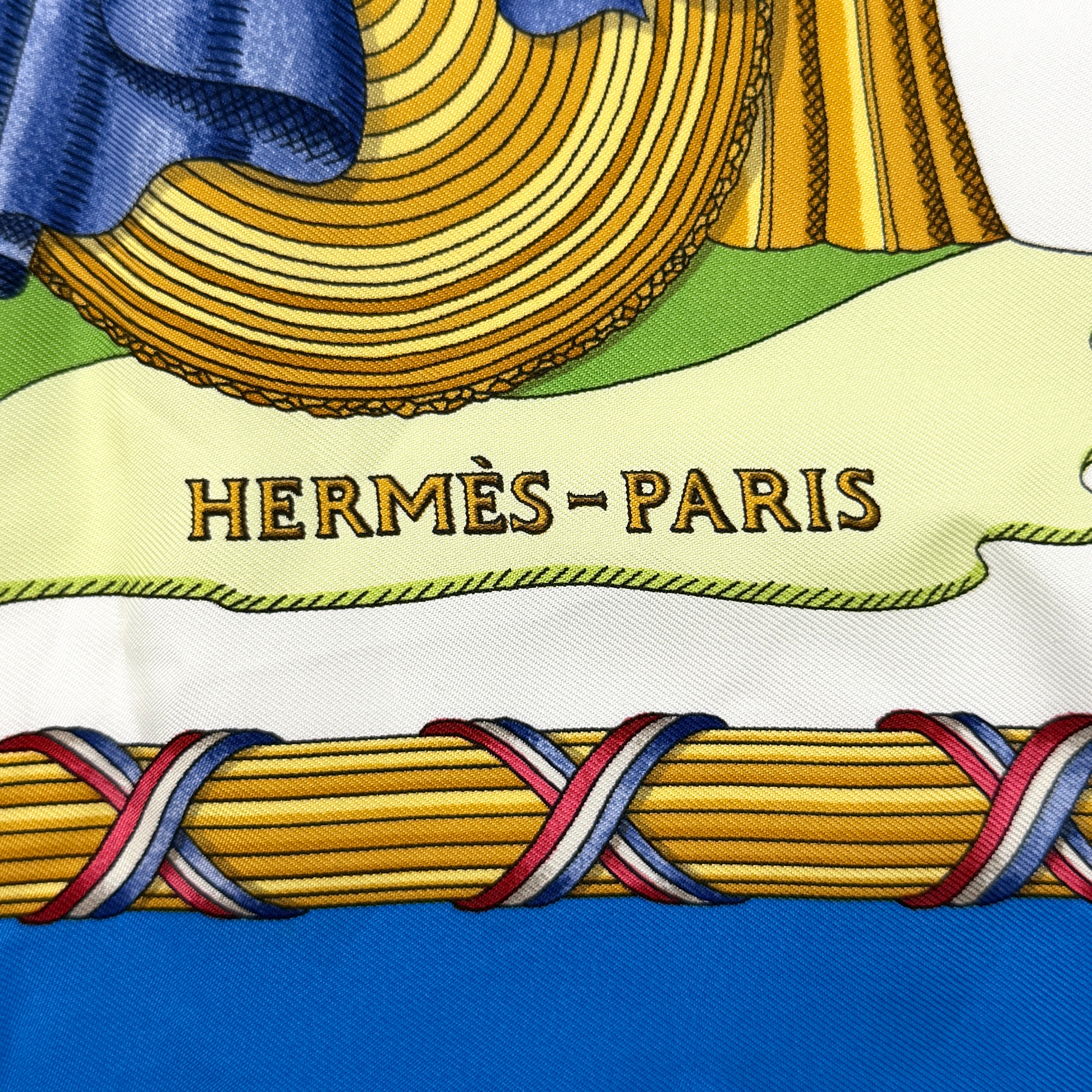 Hermès silk scarf with blue border, featuring a detailed French revolutionary motif and classical figures, shown with its signature orange box.