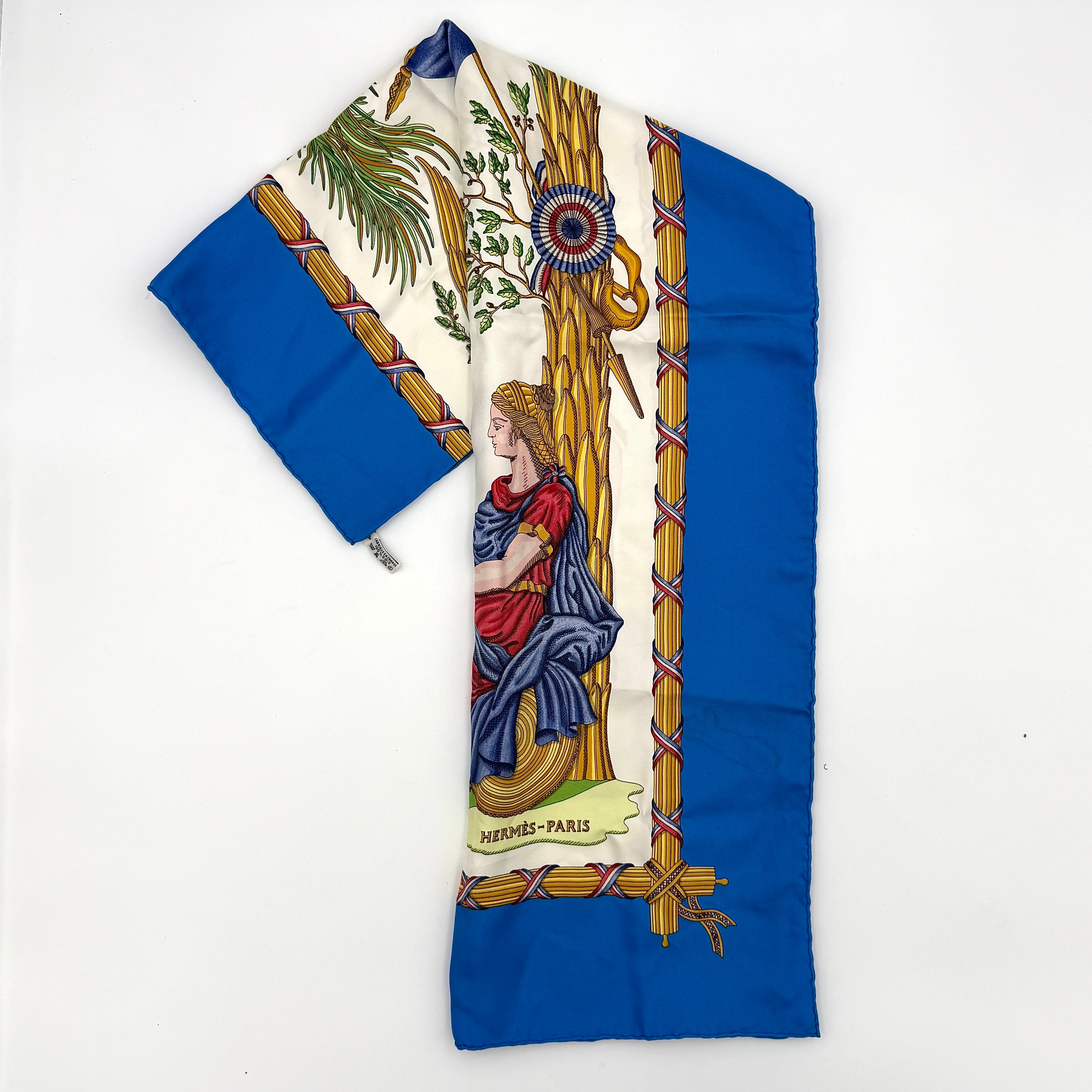 Hermès silk scarf with blue border, featuring a detailed French revolutionary motif and classical figures, shown with its signature orange box.