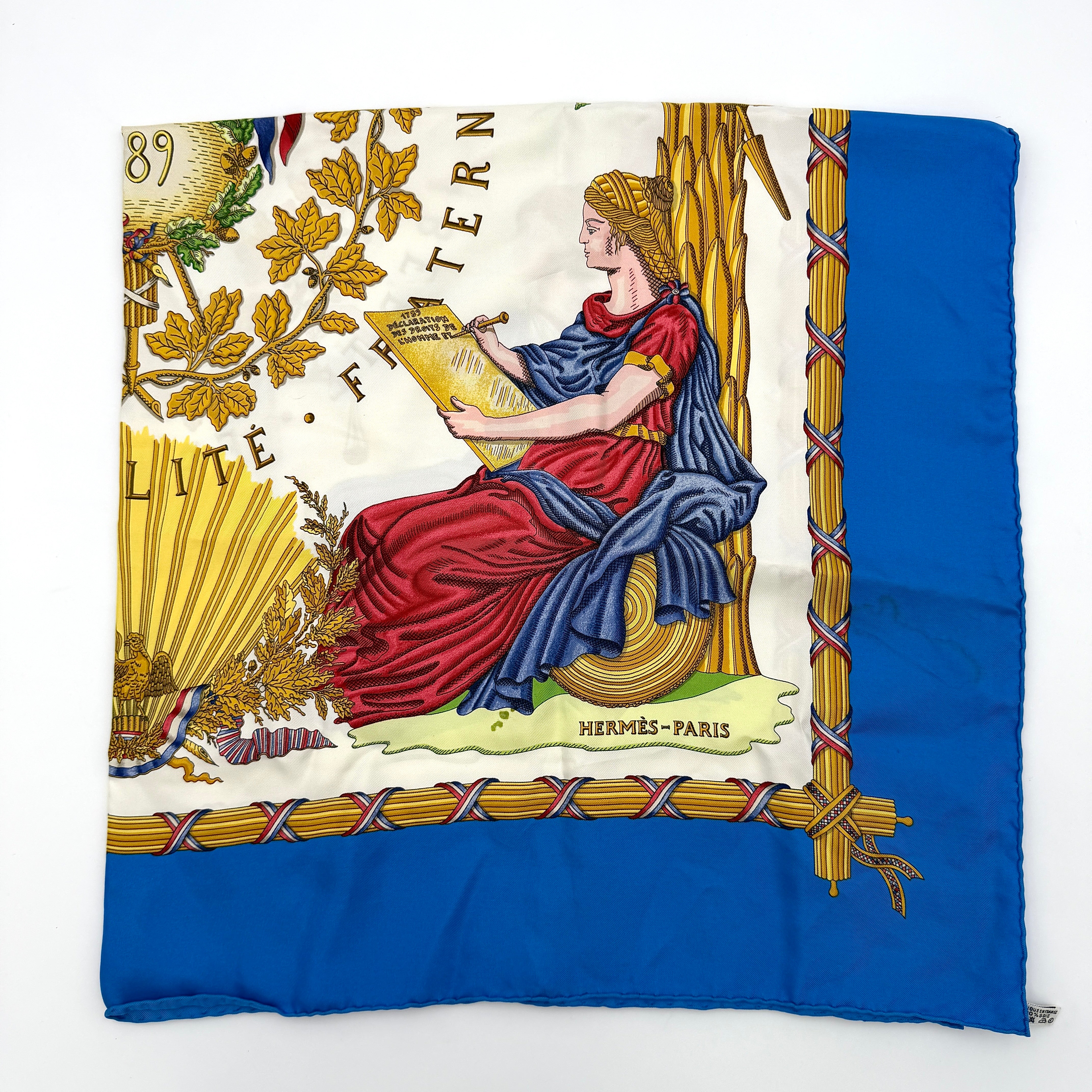 Hermès silk scarf with blue border, featuring a detailed French revolutionary motif and classical figures, shown with its signature orange box.